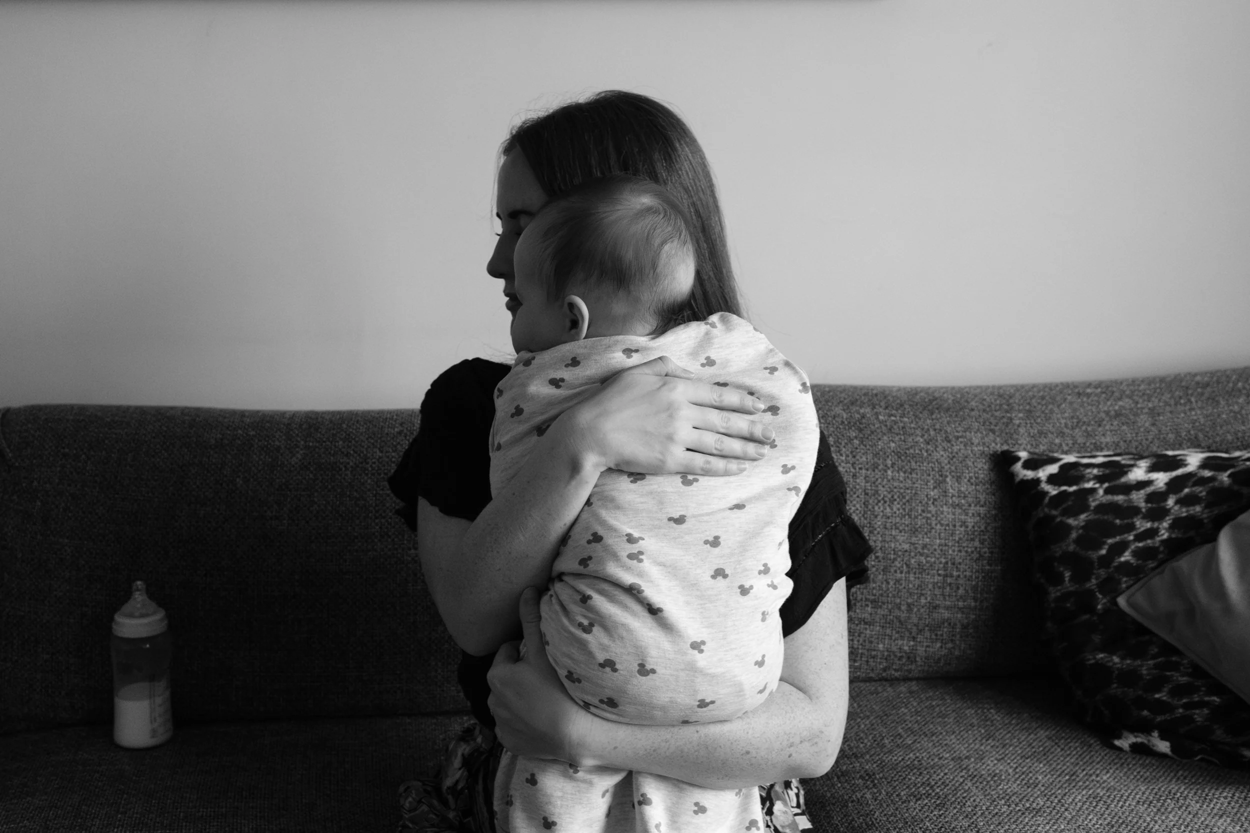 A black and white photo of a mom holdingher baby up and burping him after feeding him a bottle. Photographed by Taipei family photographer Cahleen Hudson.