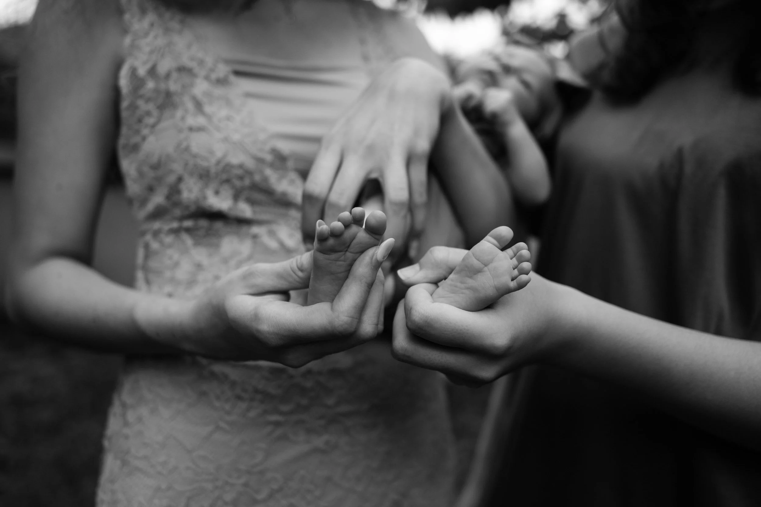 Two teenage girls are holding their newborn baby sister and grasping her tiny feet in their backyard in Taipei.