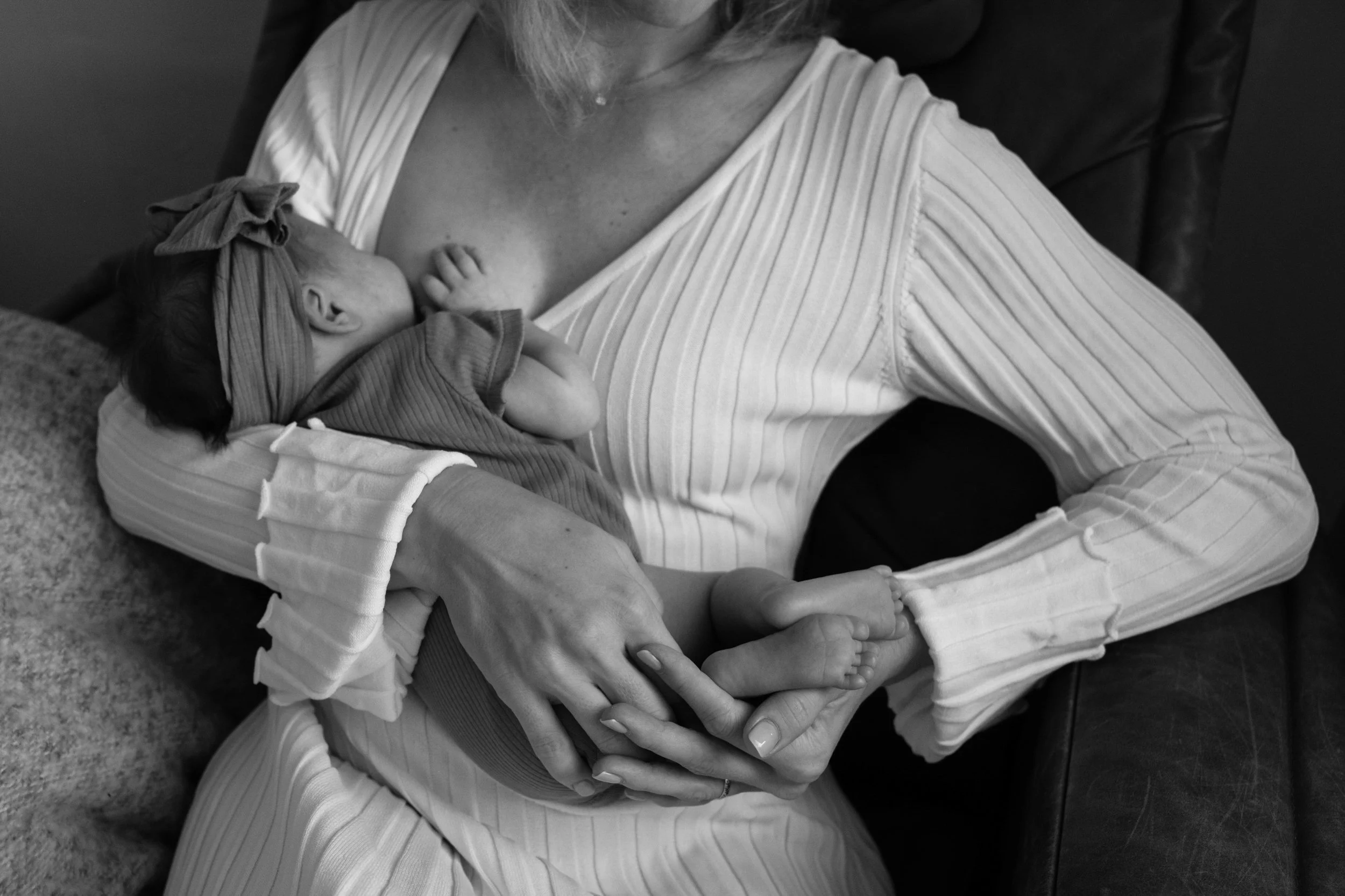 A mother is playing with her newborn baby's feet as she breastfeeds her in a rocking chair by a window in her bedroom in Taipei.