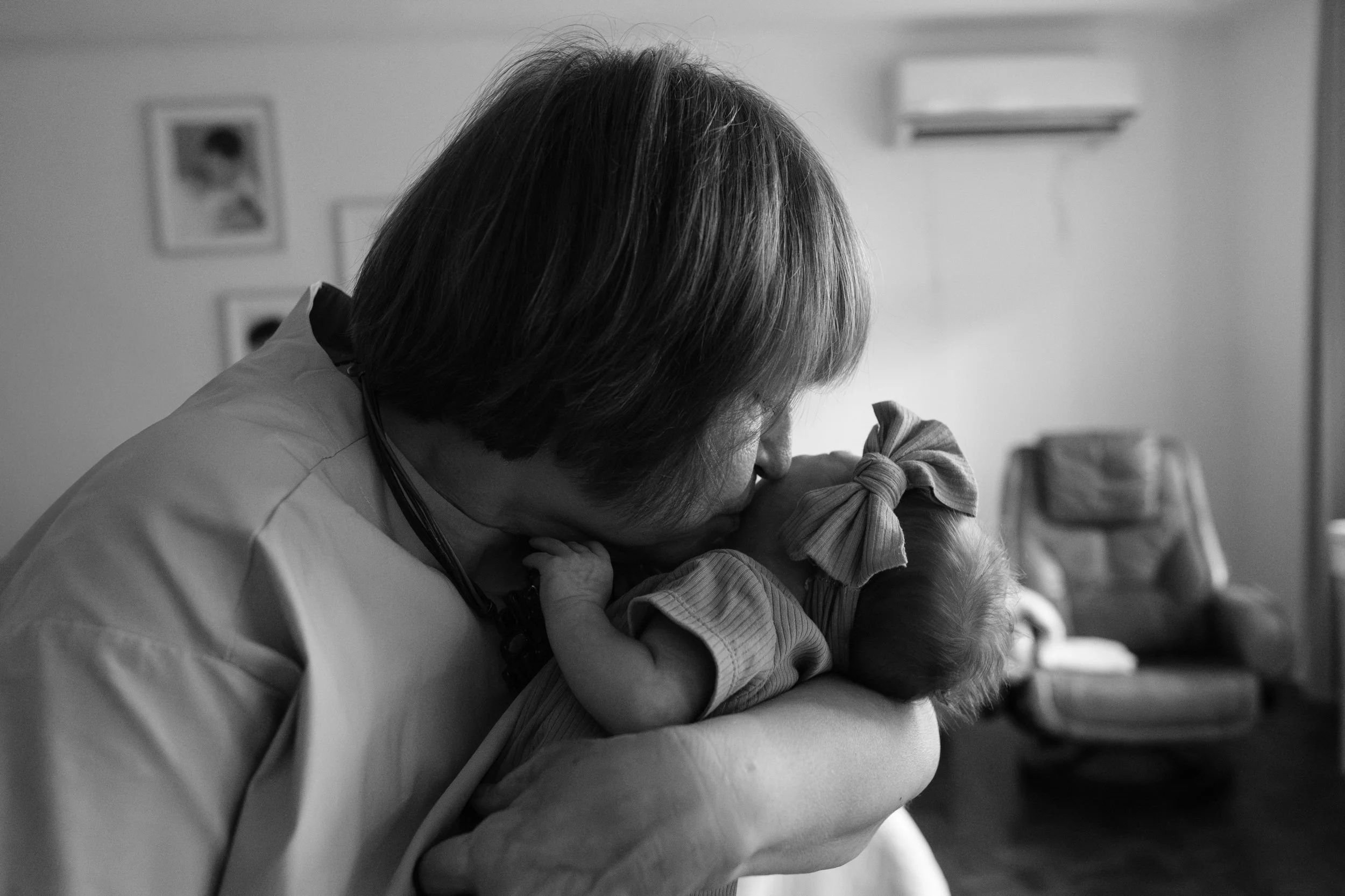A grandmother is holding her newborn granddaughter and nuuzzling the side of her face with her nose. baby grand