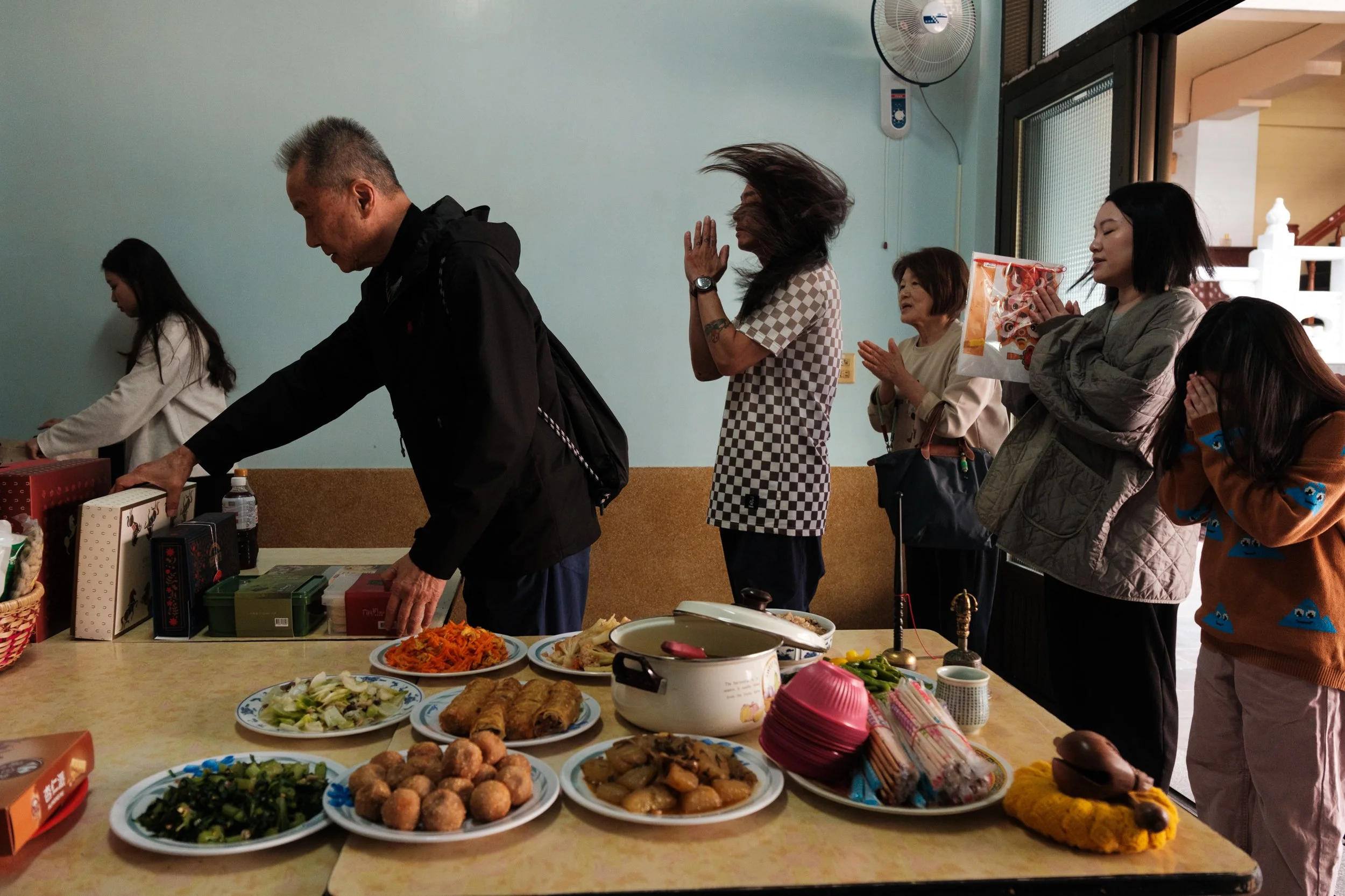 A family is bowing to an ancestral alter in a temple in Tainan, Taiwan. A table of food offerings is in the foreground. Photographed during a day in the life family photography session.