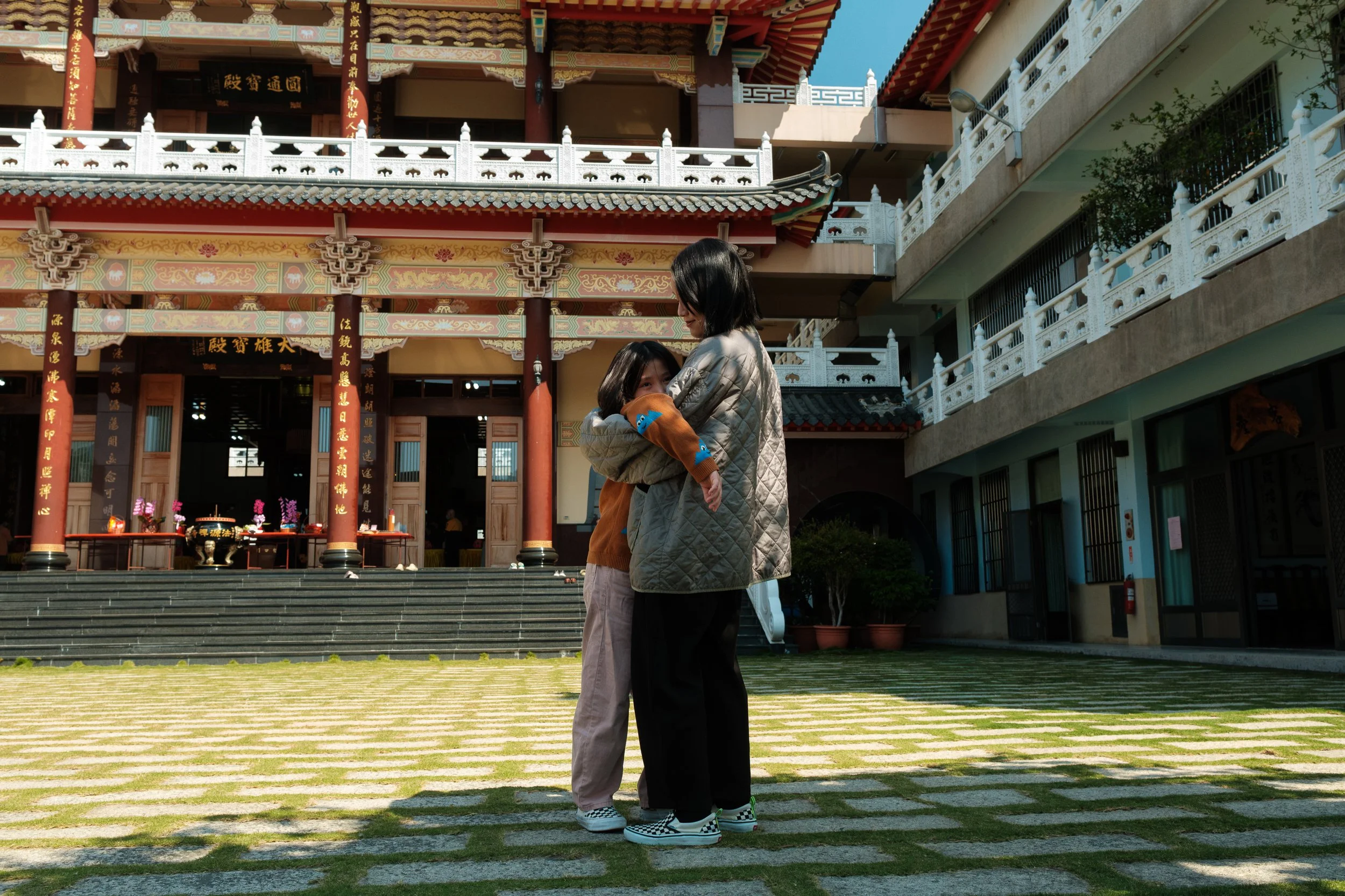 A woman is hugging her daughter in a temple courtyard in Tainan. The brightly colored temple is in the background.
