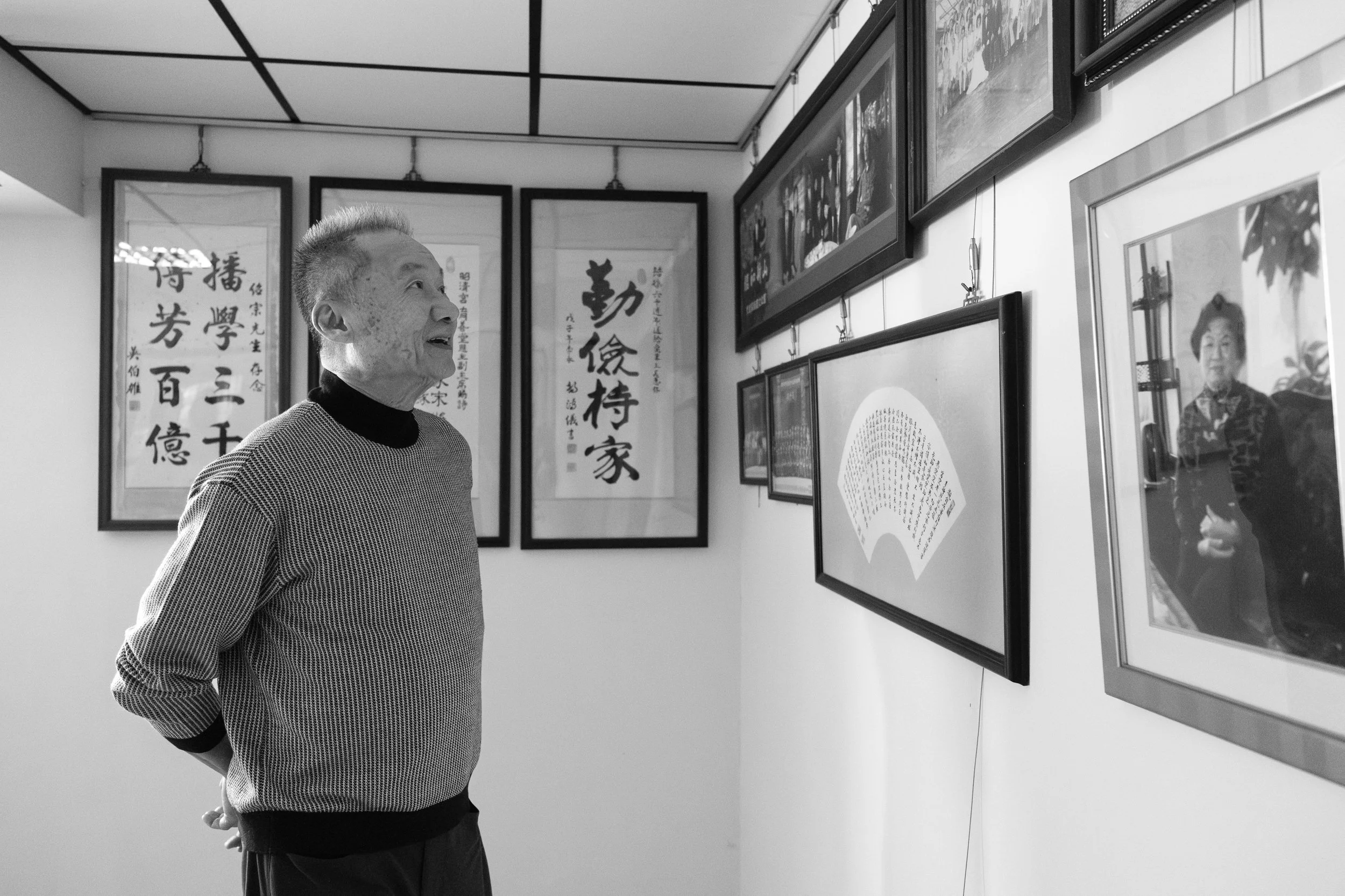An older man is looking at family photos on the wall of his ancestral home in Tainan, Taiwan. Photographed during a dcoumentary family photoshoot by Taipei photographer Cahleen Hudson.