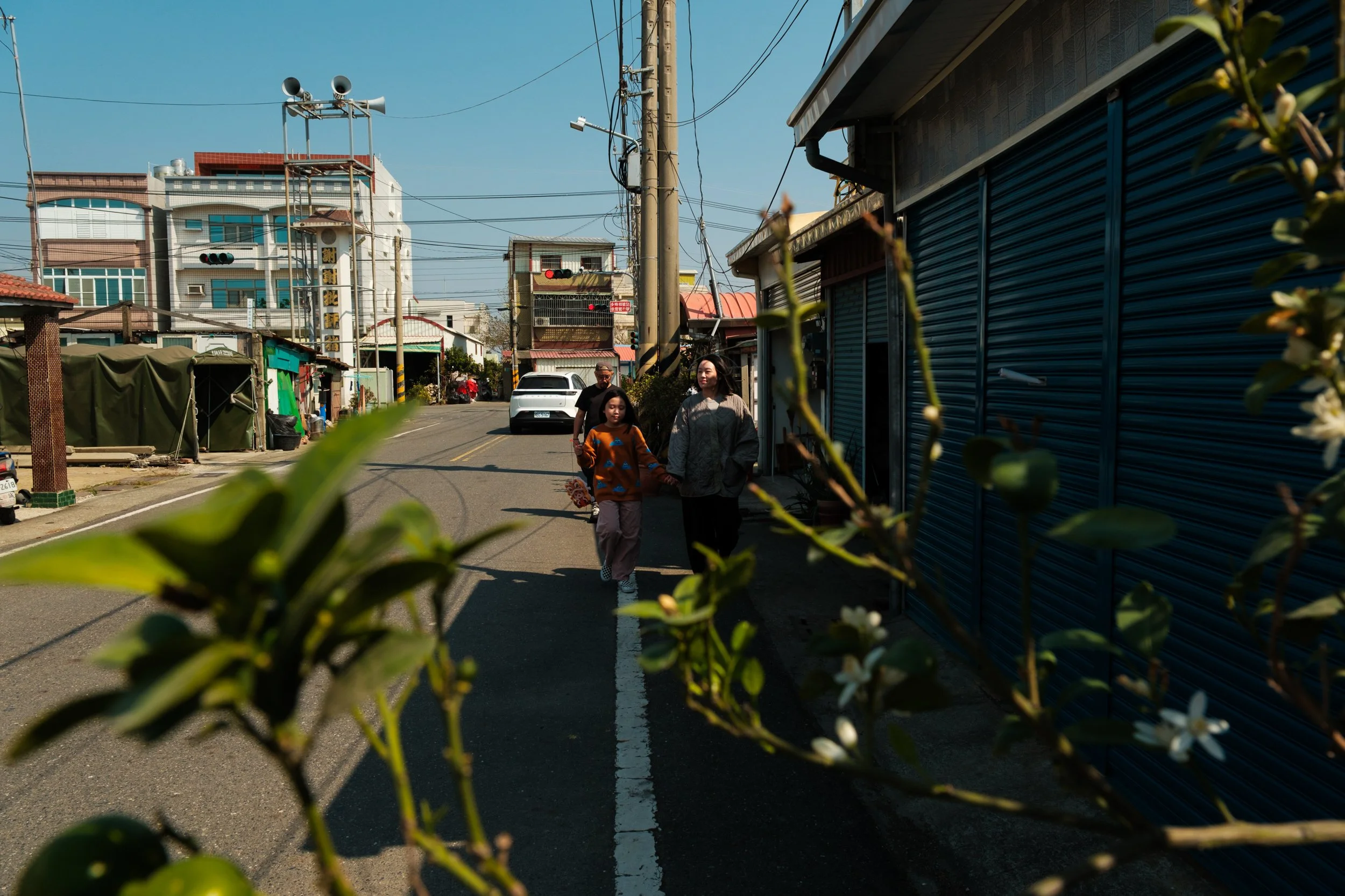 A family walks down a street in Tainan on a sunny day. A candid moment during a vacation family photography session.
