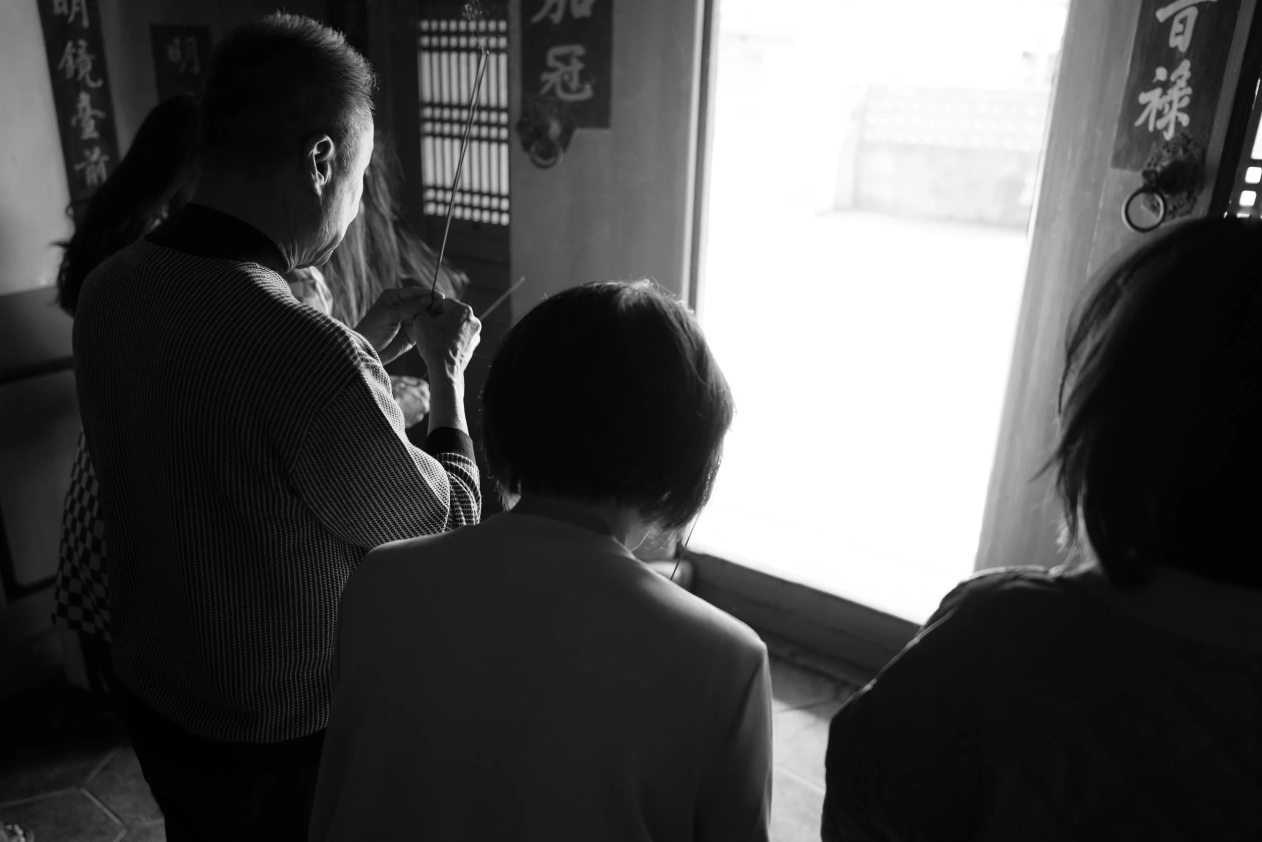 A family is holding incense and bowing towards an open door in their ancestral home in Tainan, Taiwan. A candid documentary family photography photo from a day in the life session.