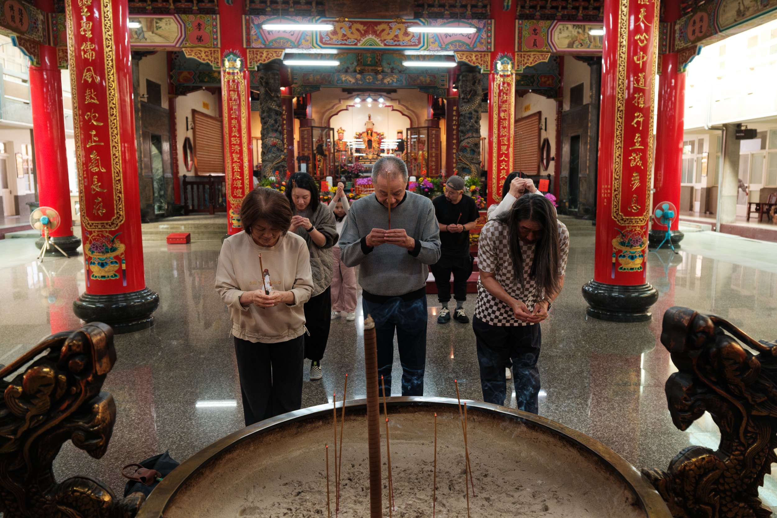 A family bows together before an alter with incense at a temple in Tainan, Taiwan. Photographed during a vacation family photoshoot by Taipei photographer Cahleen Hudson.