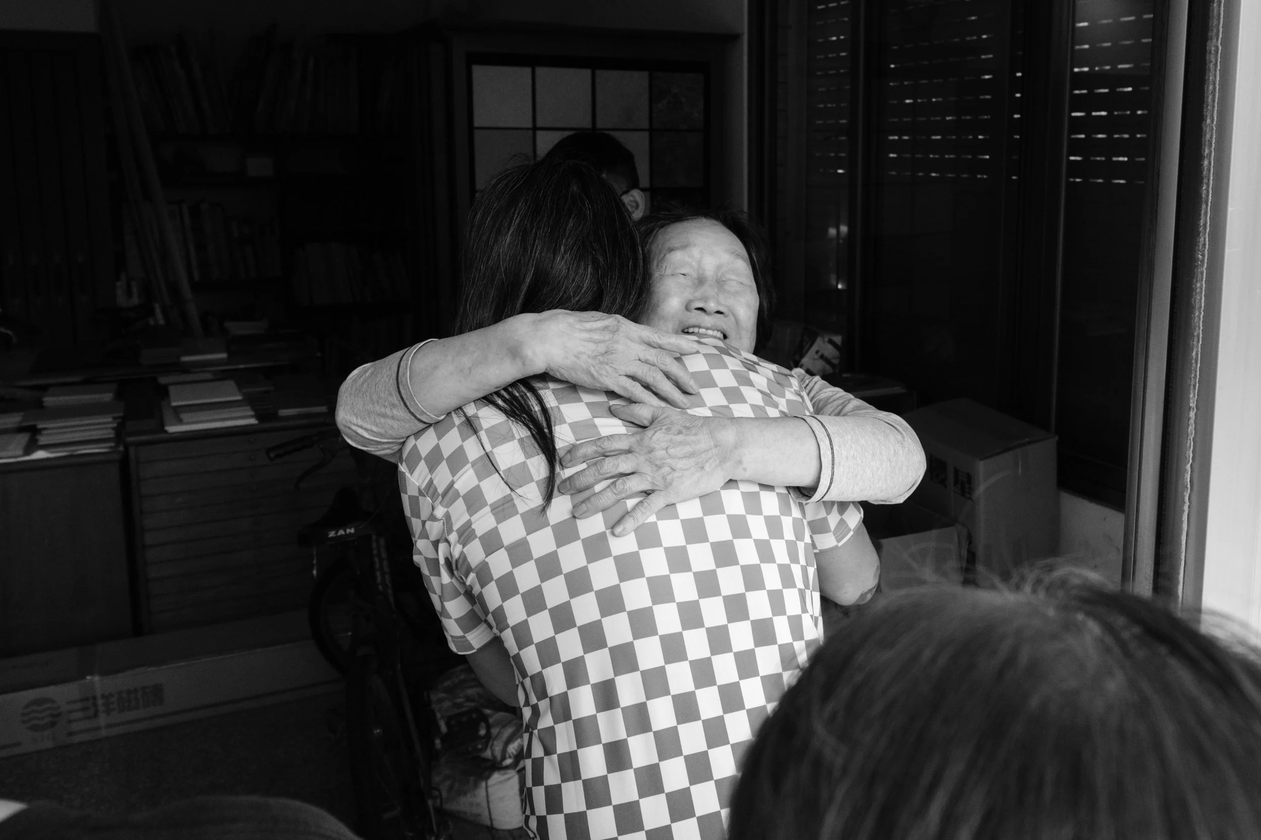 A woman's face can be seen over a man's shoulder as she reaches up to hug him. She's smiling and her eyes are closed. A natural family moment of connection.