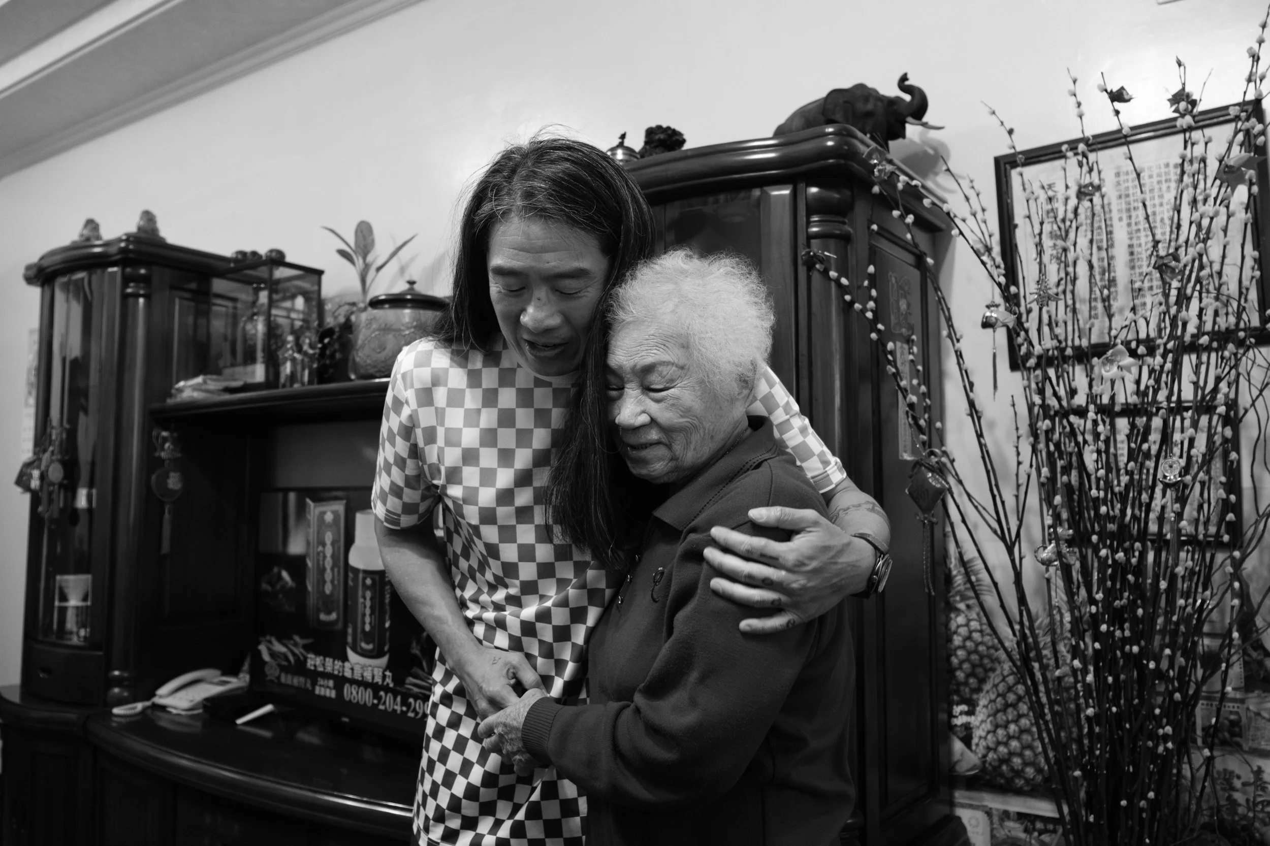 A man hugs an old woman from the side in their ancestral home in Tainan during Chinese New Year. Photographed by Taipei family photographer Cahleen Hudson.