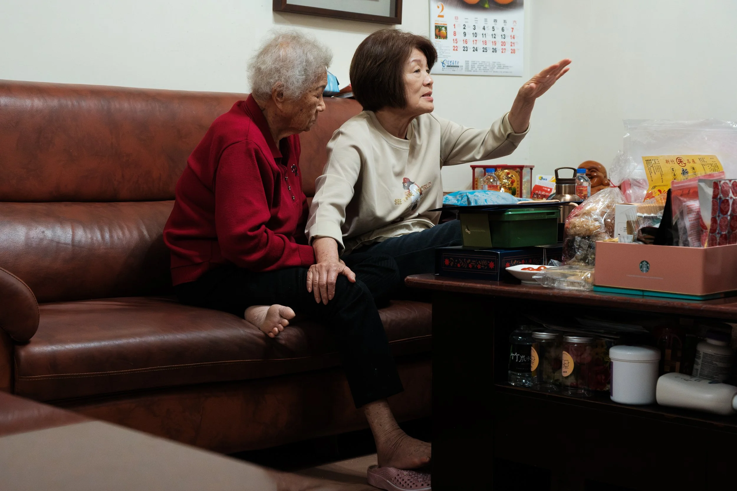 A woman is sitting close to her mother on a sofa and touching her mother's leg. A heartwarming moment captured during a natural in-home family photoshoot by Taipei photographer Cahleen Hudson.