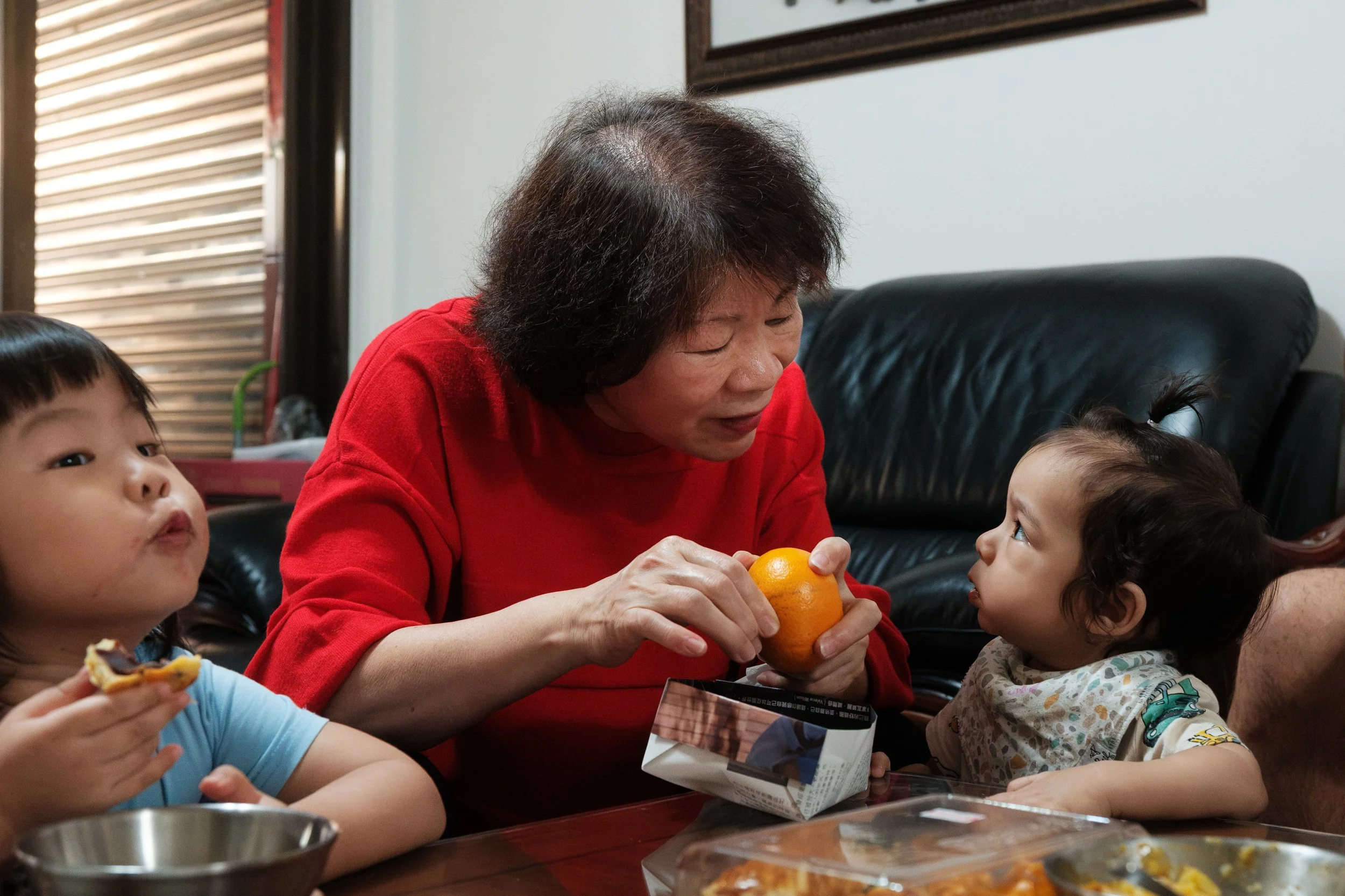 An older woman is peeling an orange for her baby grandson in her home in Tainan during a family gathering for Chinese New Year. Photographed by Taipei photographer Cahleen Hudson.