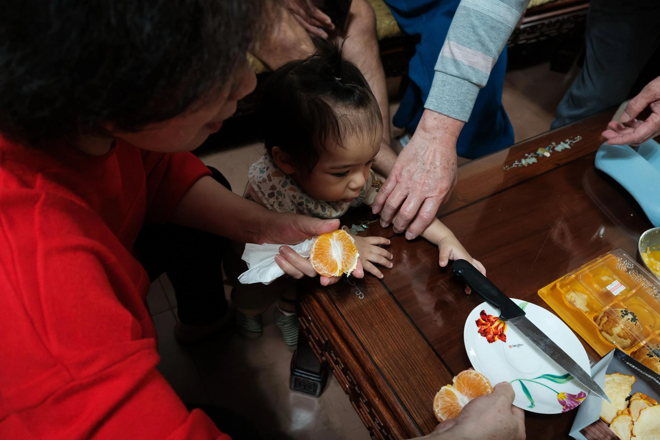 A grandfather is grabbing his baby grandson's hand and stopping him from grabbing a knide lying on a table. A funny, candid moment from a documentary family photoshoot.