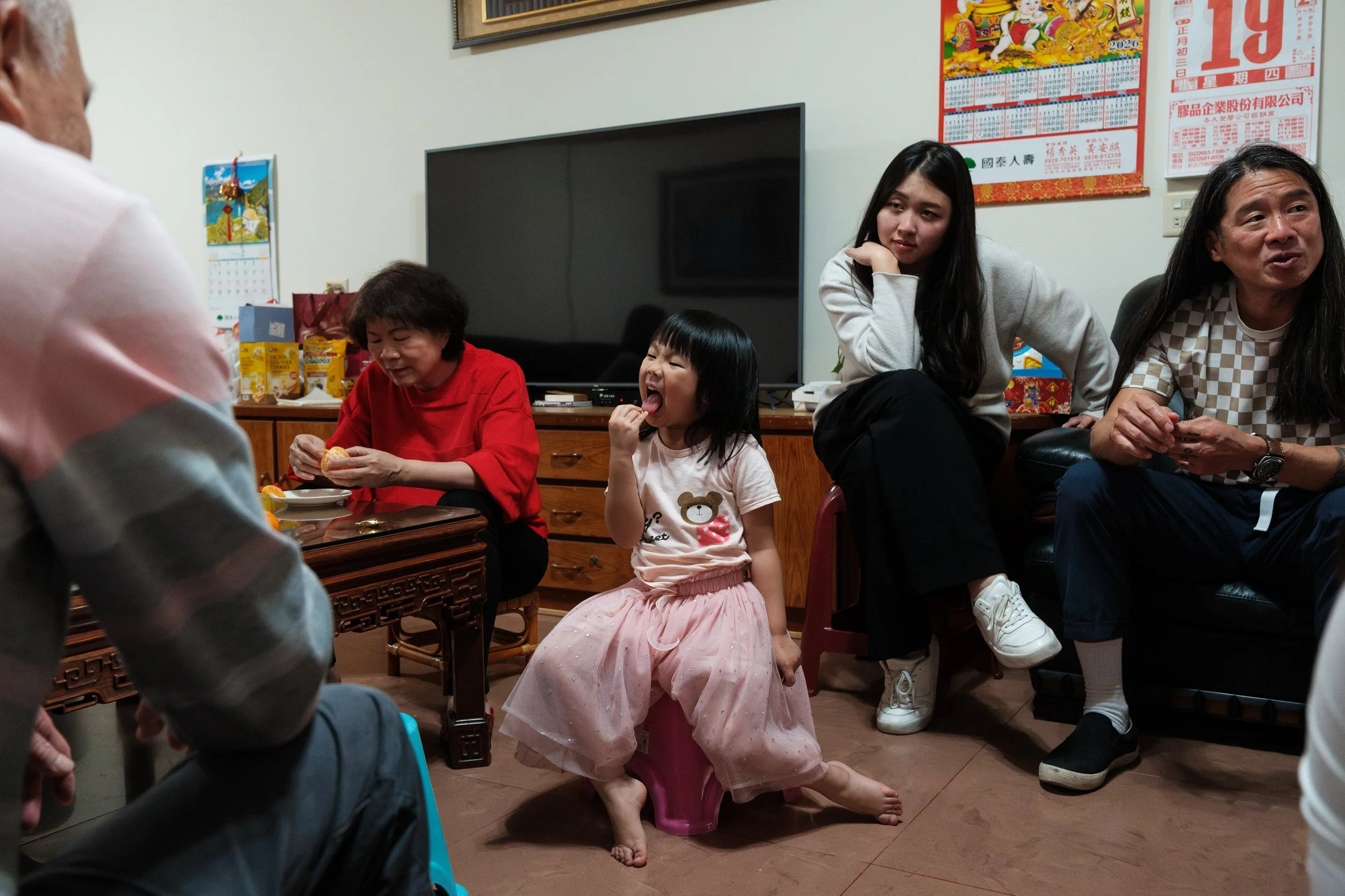 A little girl is making a funny face and sticking her tongue out as she eats an orange slice during a family gathering in Tainan. Photographed during an in-home family photography session.