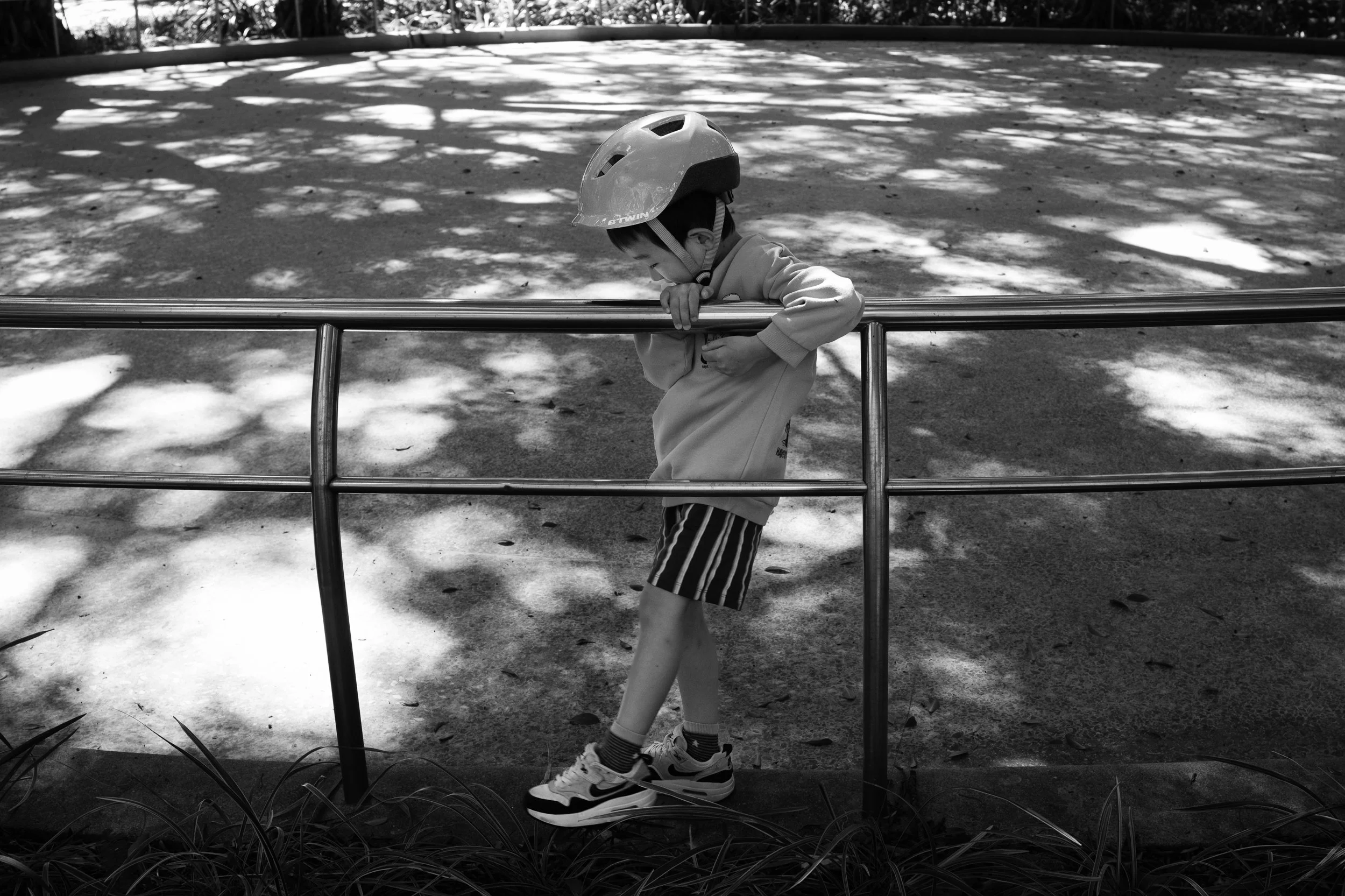 A little boy isleaning on the railing of the skating rink at a Tienmu park during a Taipei outdoor family photoshoot.