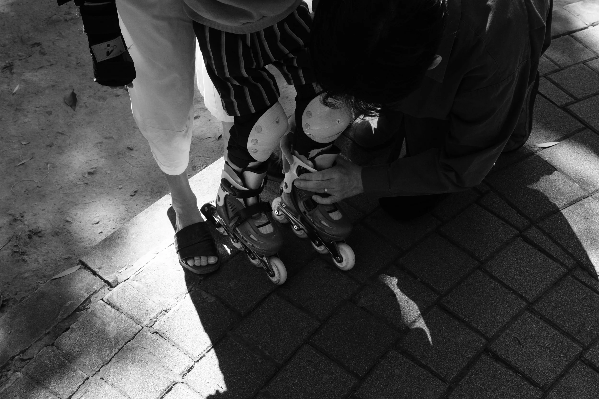 Two people are helping a small child put on rollerblades at a park in Tienmu, Taiwan, Photographed during an outdoor family photoshoot.