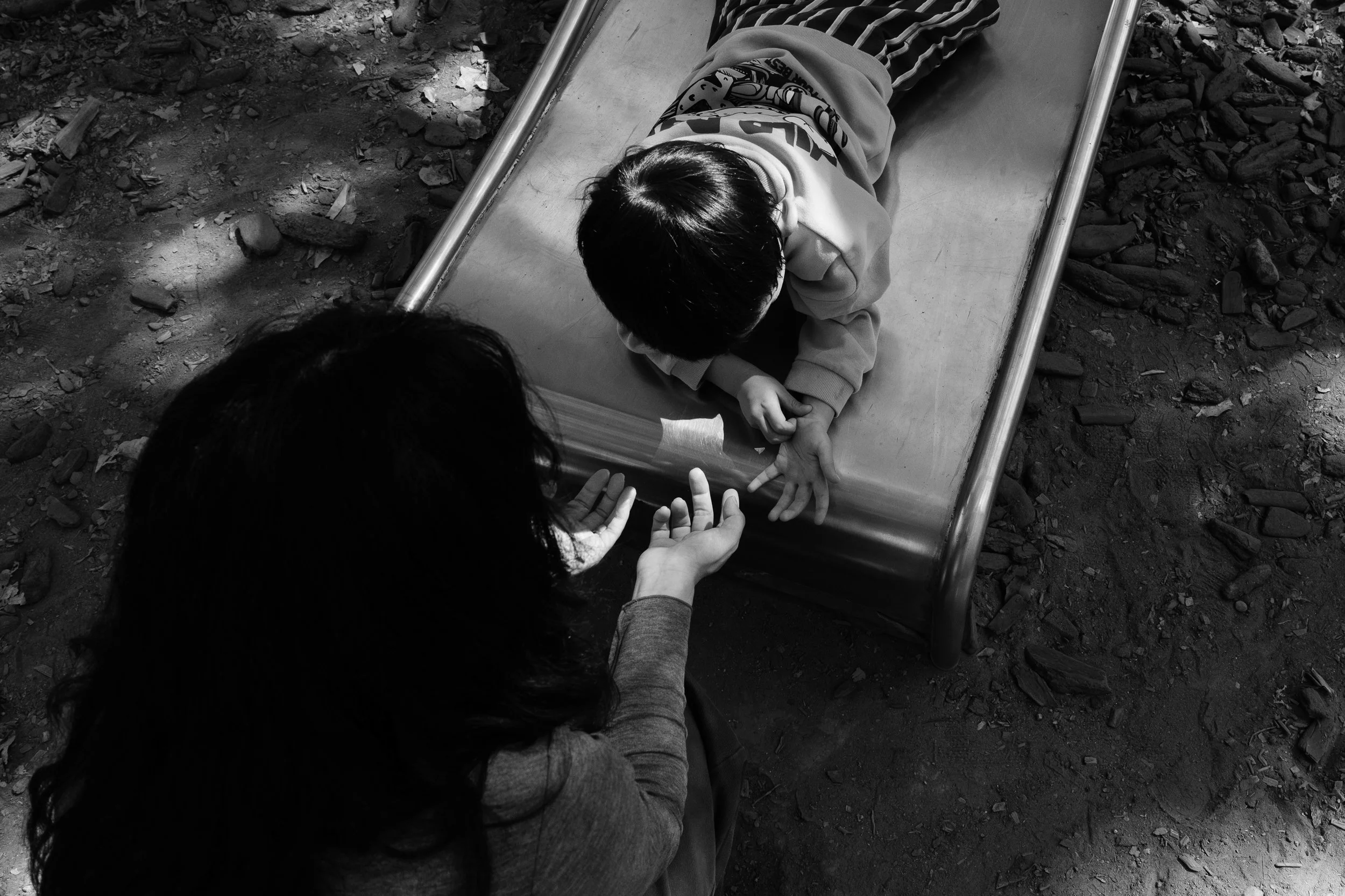 A mother is holding her son's hand after he slides to the bottom of a slide at a park in taipei, Taiwan during an outdoor family photoshoot.