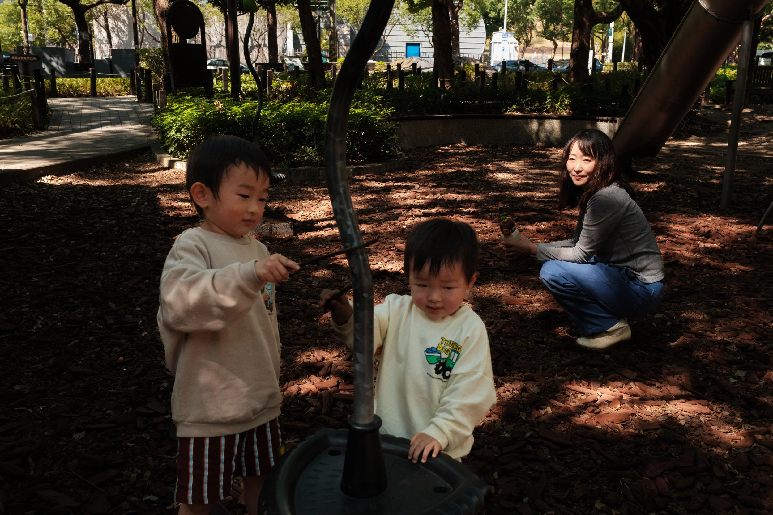 Two boys are playing in a Tienmu park as their mother watches them in the background. Photographed by Taipei photographer Cahleen Hudson during an outdoor family photoshoot.