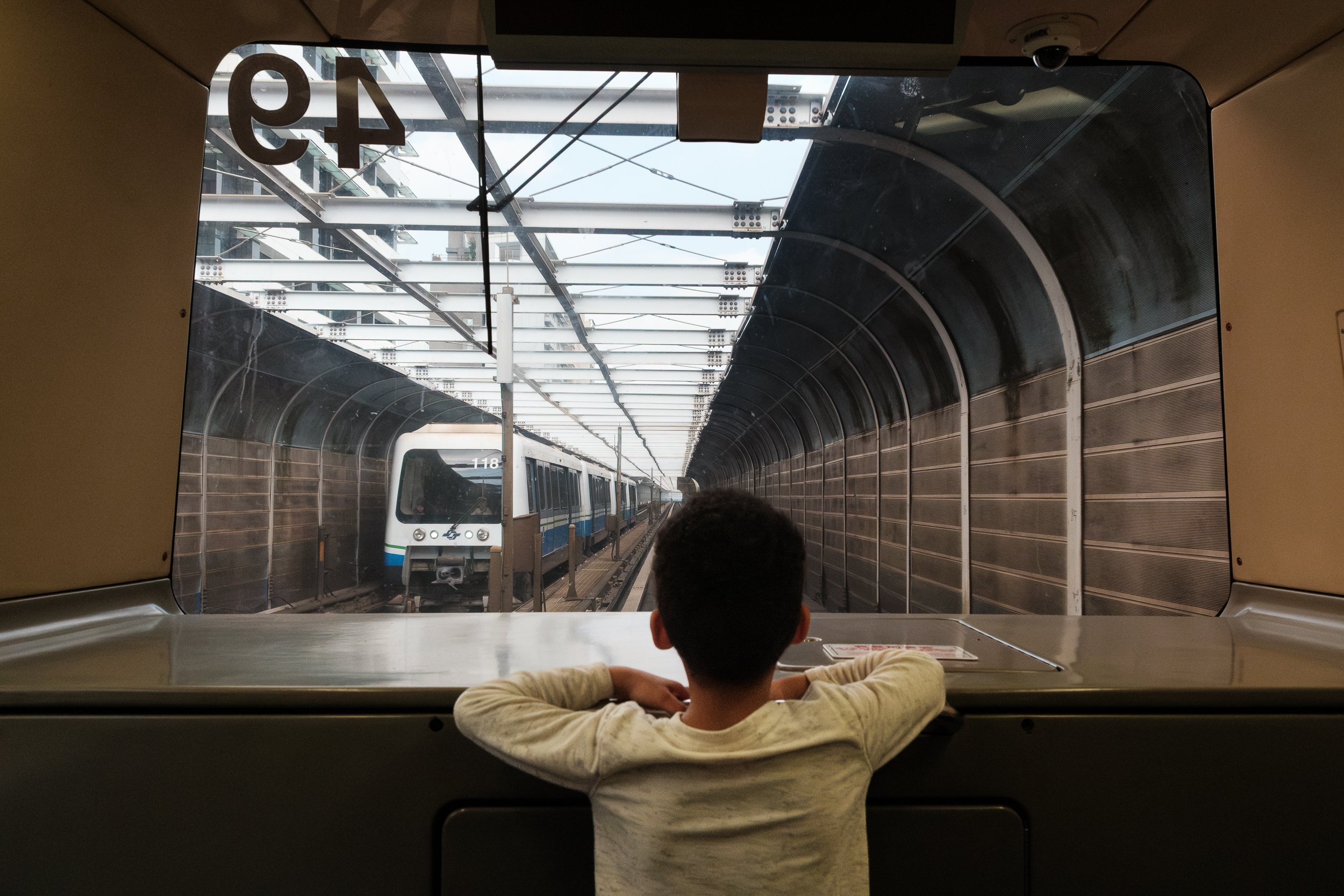 A little boy is in the front car of the brown line of the Taipei MRT and watching another MRT car about to pass by him. Photographed by Taipei family photographer Cahleen Hudson.