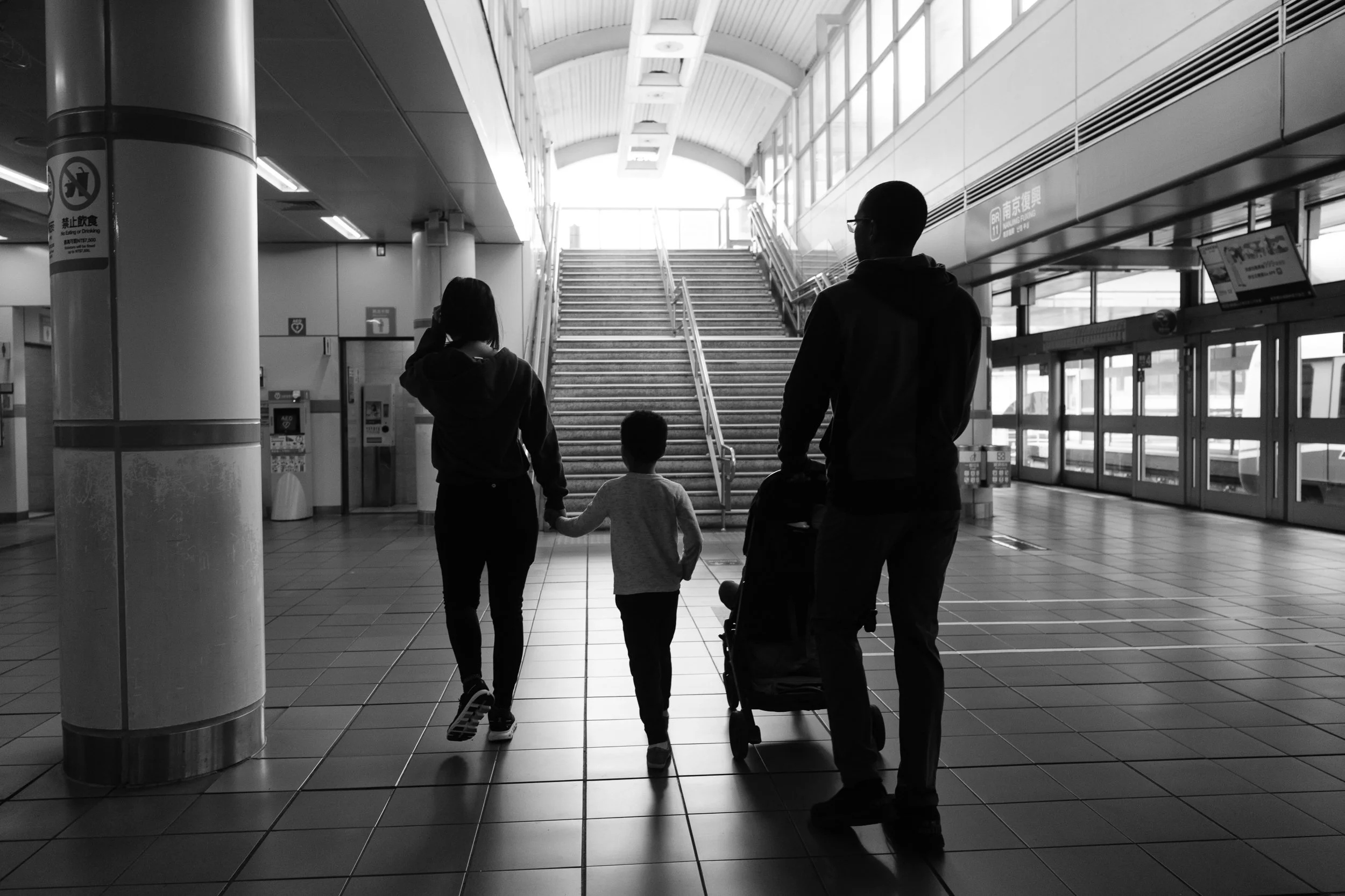 A family of four is walking in a Taipei MRT station during a family photoshoot. The photo is from behind. 
