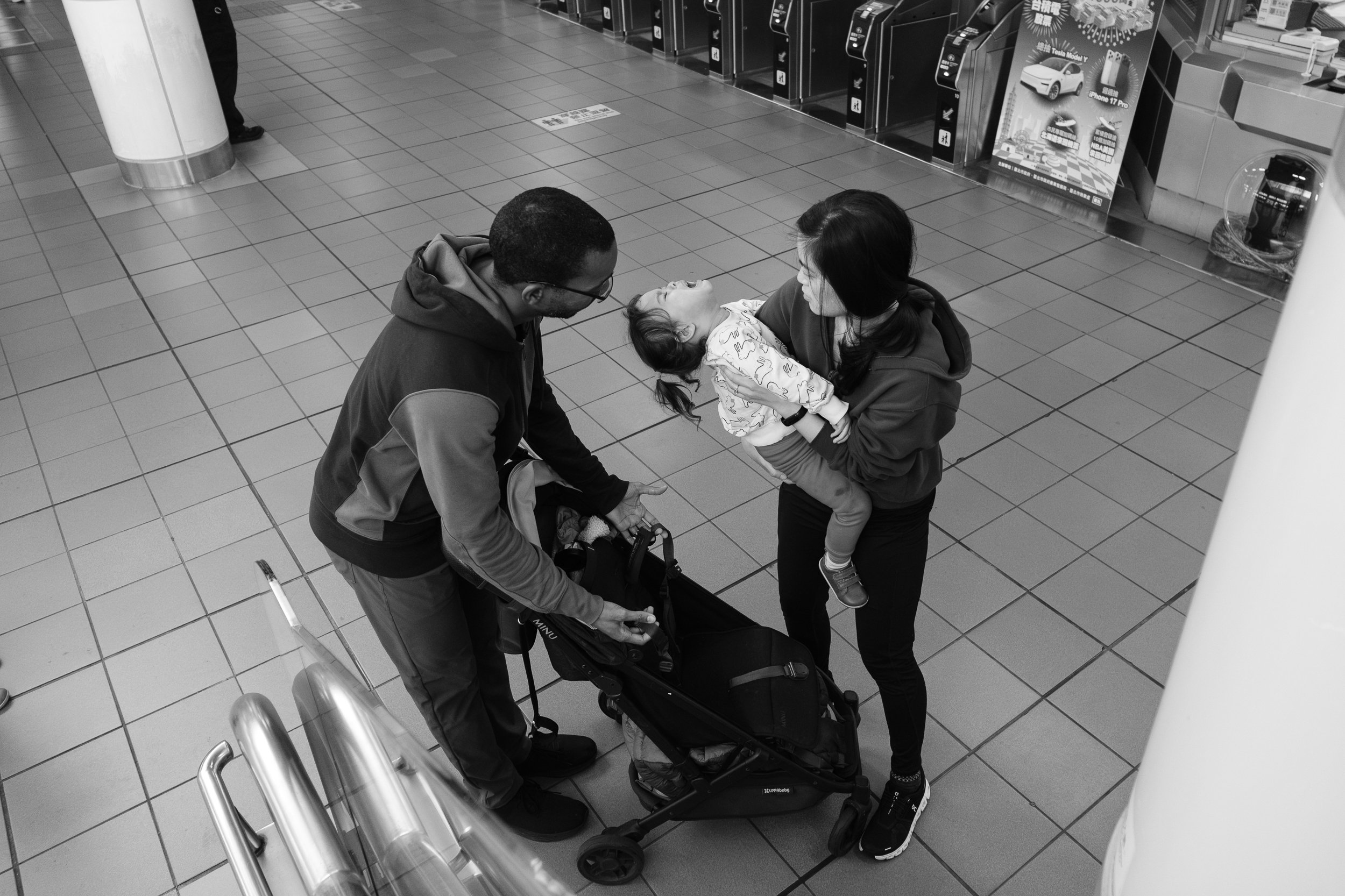 Two parents are trying to put a crying child into a stroller at a Taipei MRT station during an outdoor family photography session in Taiwan.