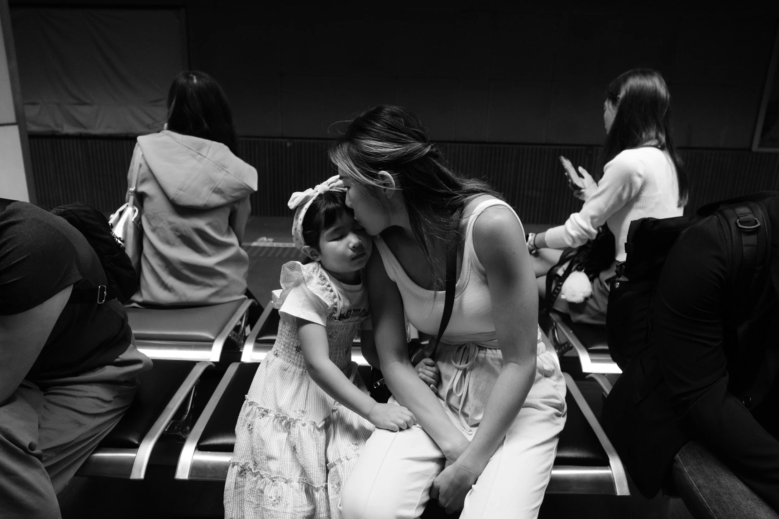 A mother kisses the top of her daughter's head as they wait for their train to arrive at a Taipei train station. Photographed by Taipei family photographer Cahleen Hudson.