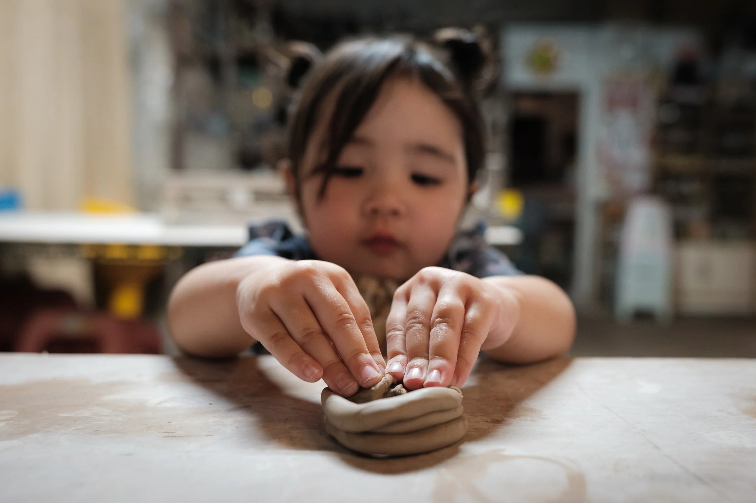 A close-up of a little girl's fingers pinching clay as she makes a bowl in a shop in Yingge during an outdoor family photography session in Taiwan.