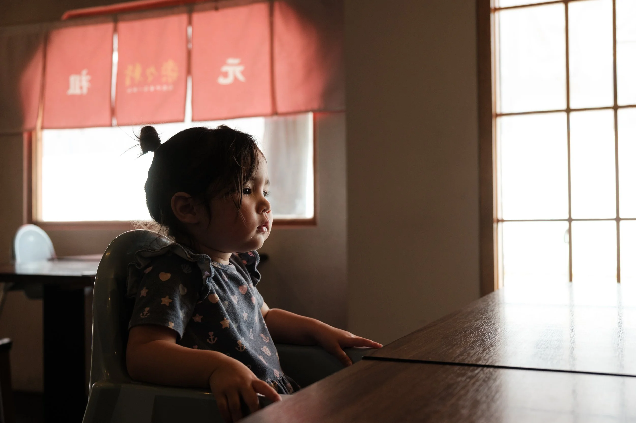 A little girl is sitting in a restaurant on Yingge Old Street, waiting for her food. Photographed during an outdoor documentary family photography session.