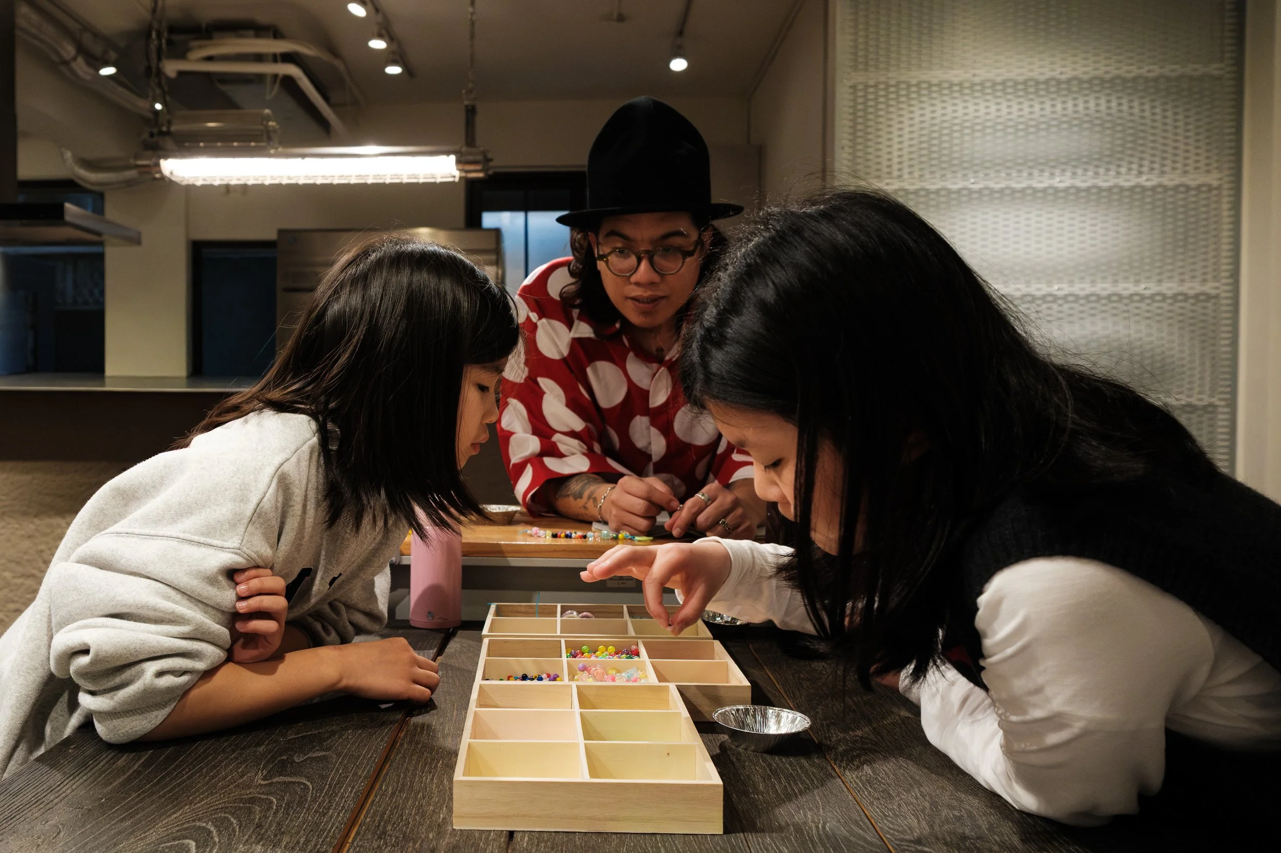 A man helps two young girls make beaded bracelets at a bracelet beading station at a child's birthday party in Daain, Taipei.