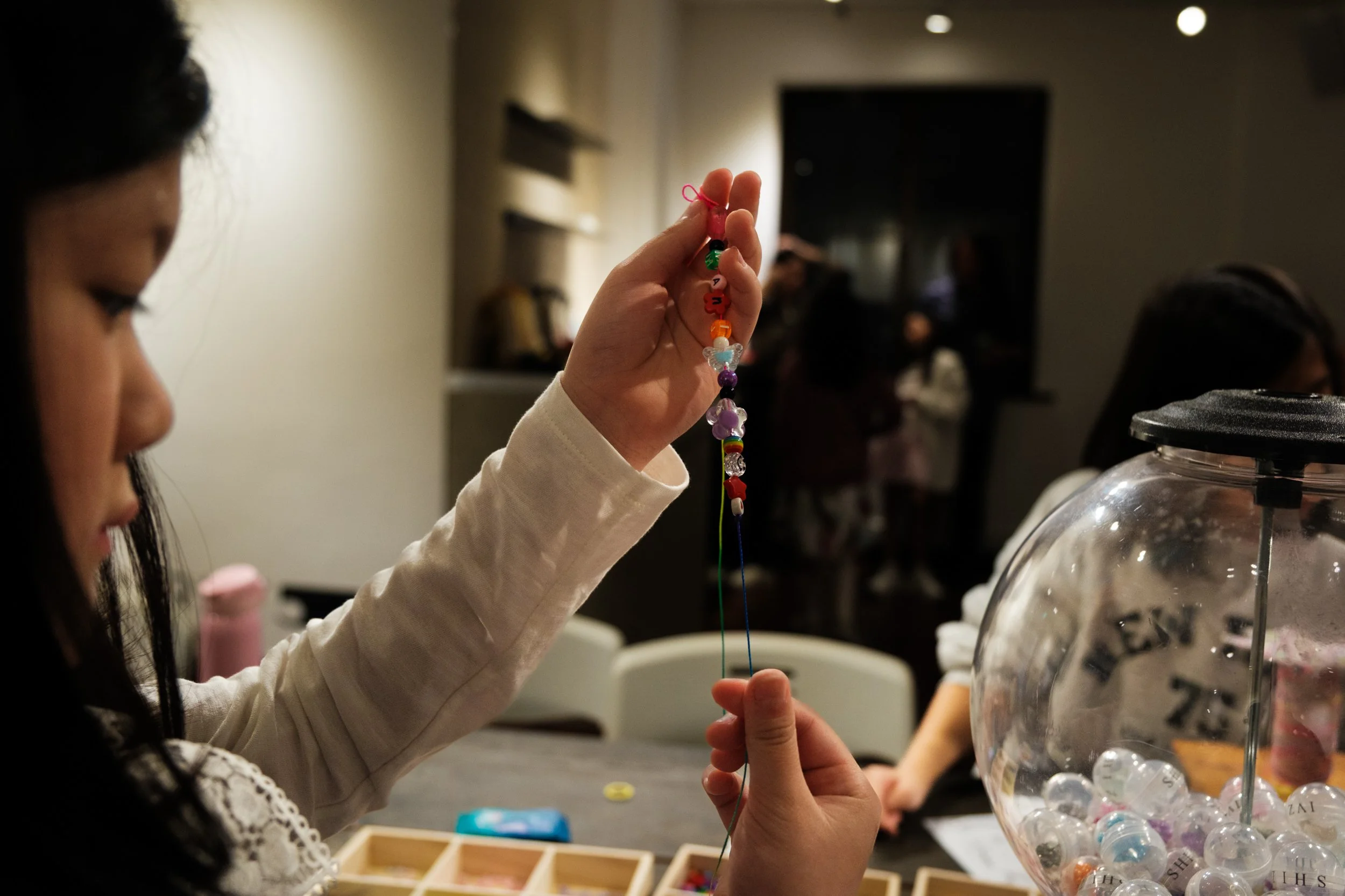 A little girl holds up the beaeed bracelet she's making at her friend's 9th birthday party at MRKT5 in Taipei.