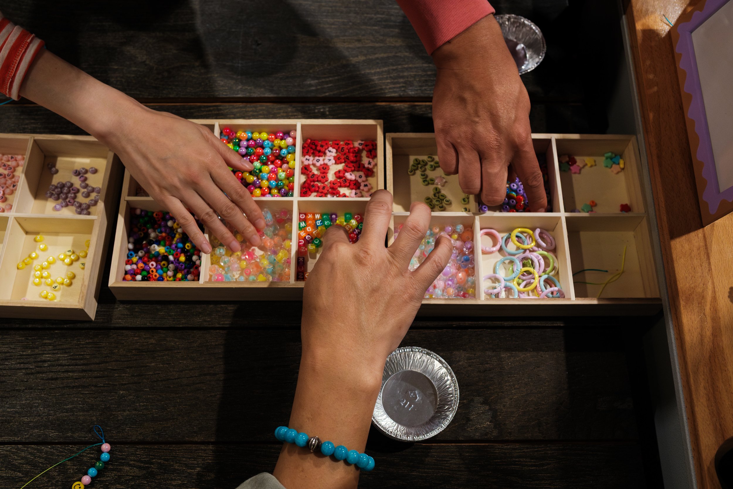 A close-up image of hands reaching for beads that are organized by color in a wooden box. Photographed by taipei family photographer Cahleen Hudson at a kid's birthday party.