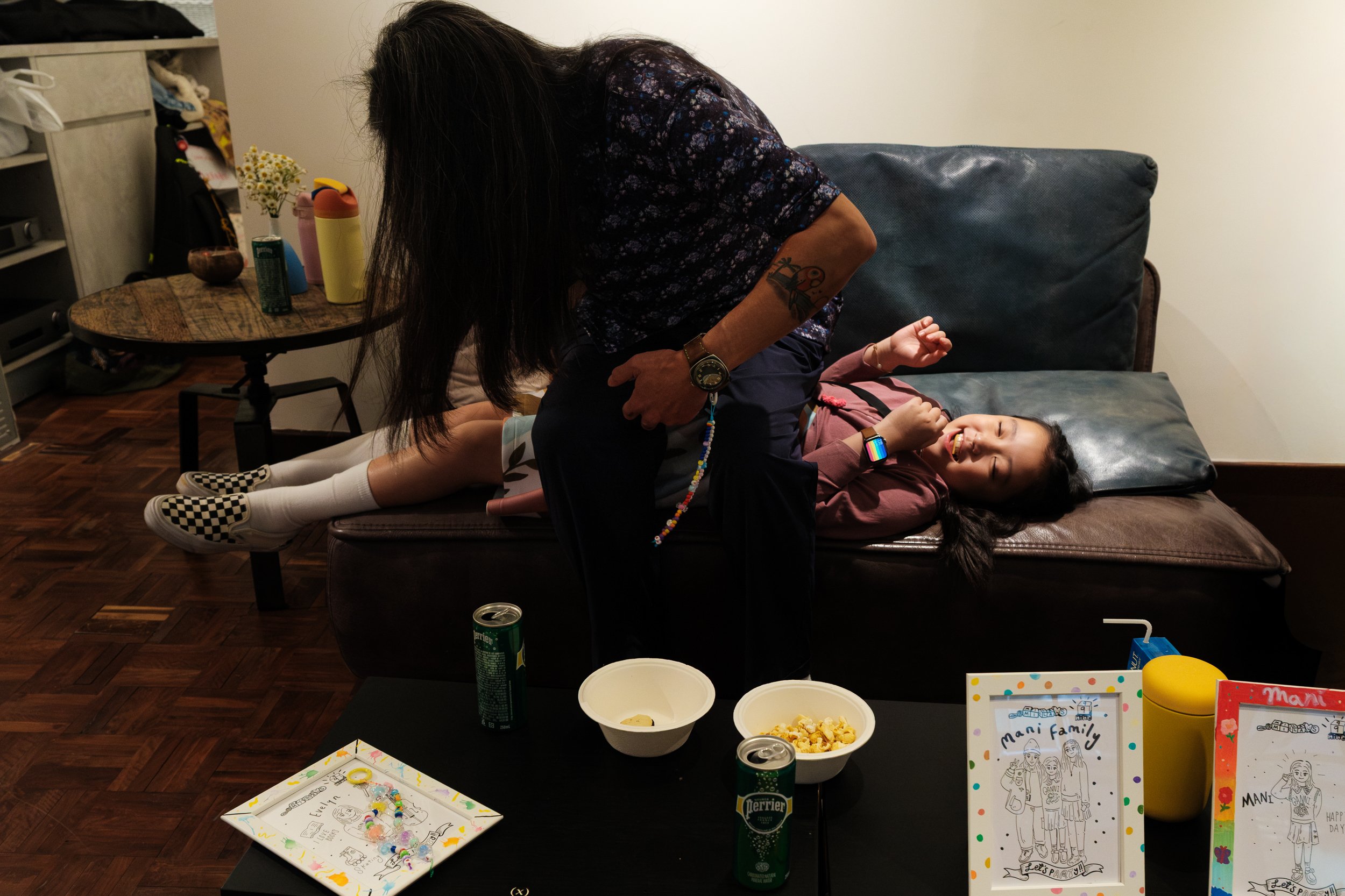 An uncle is jokingly sitting on his niece, who is lying on a couch at MRKT5 in Daan, Taipei during her 9th birthday party.