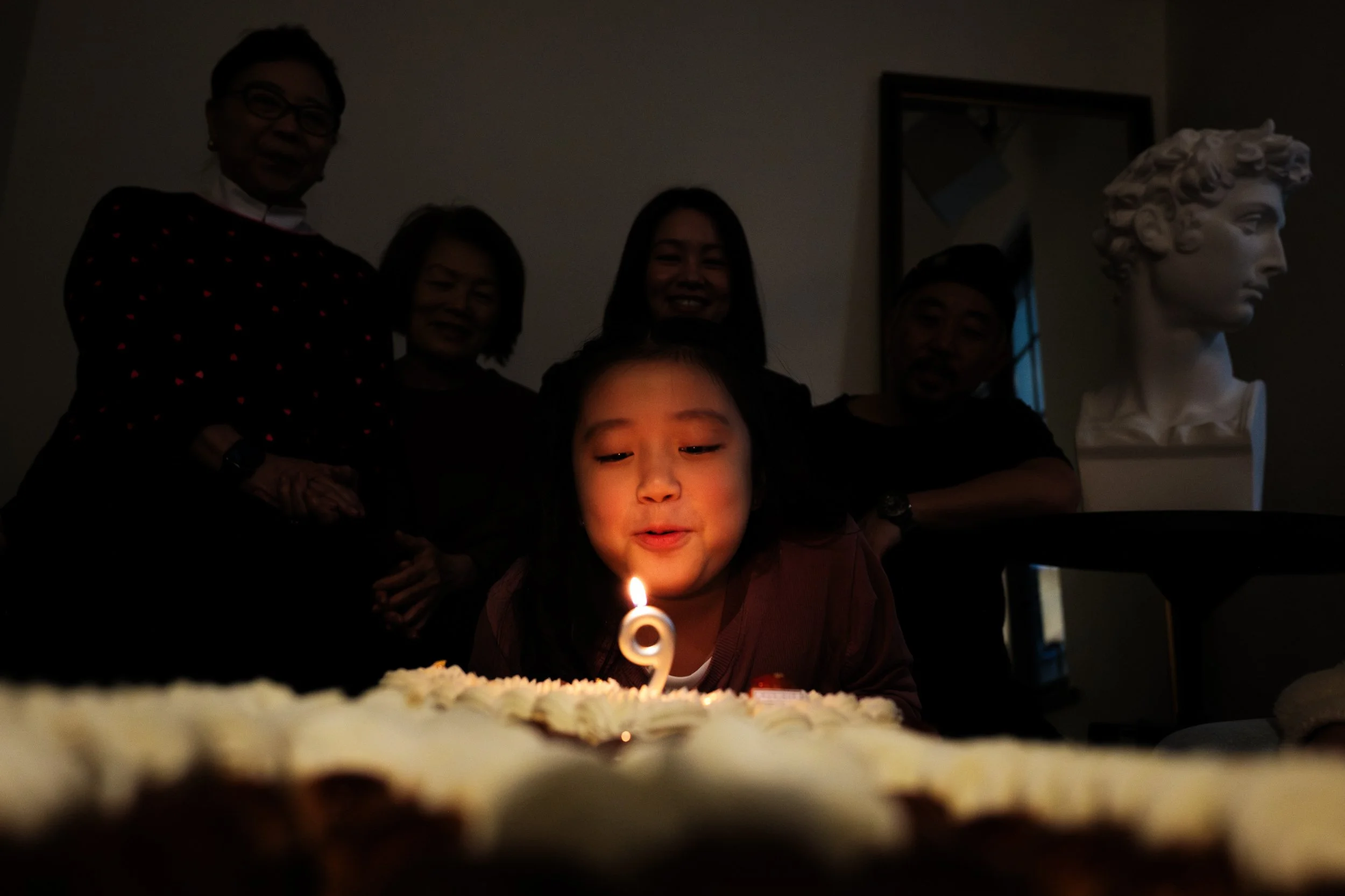 A little girl's face is illuminated as she leans over a lit birthday candle on her birthday cake during her party in Taipei.