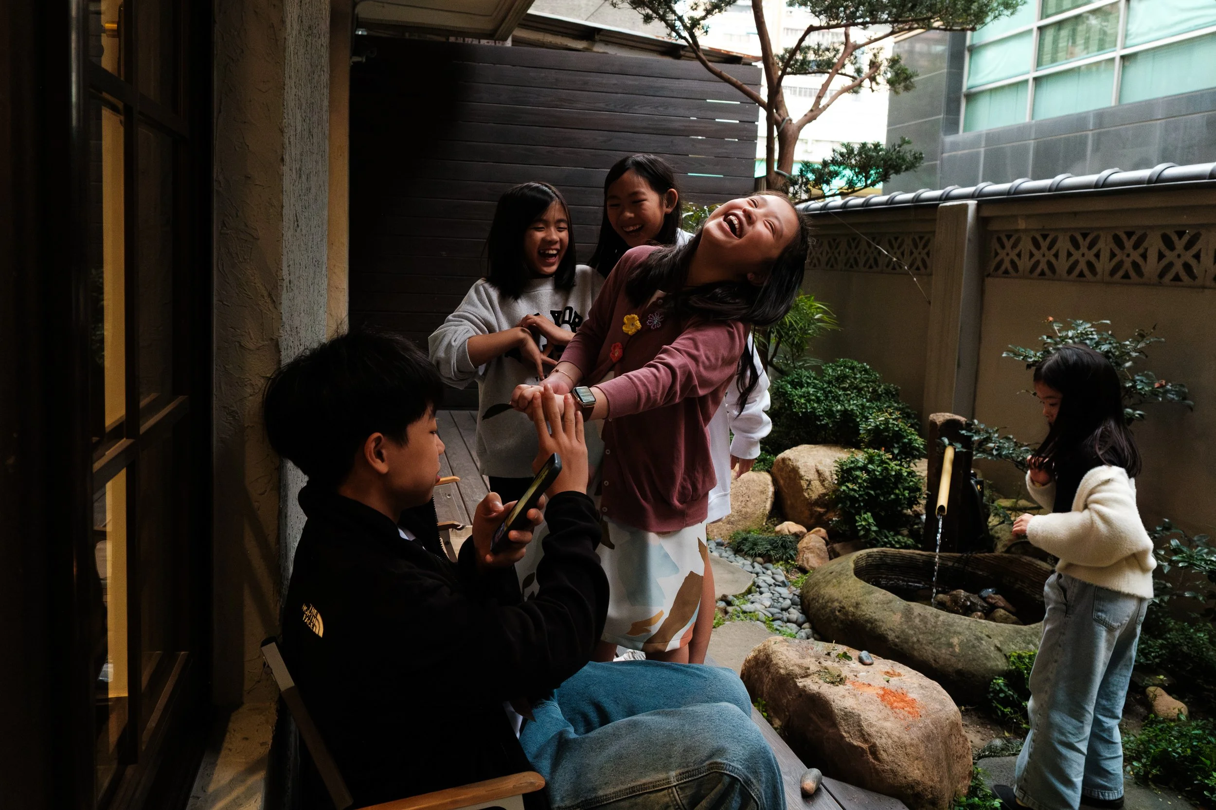 A young girl and her friends is laughing as she serves a cup of mashed up leaves to a teenage boy. They are outside during her birthday party in Taipei, Taiwan.