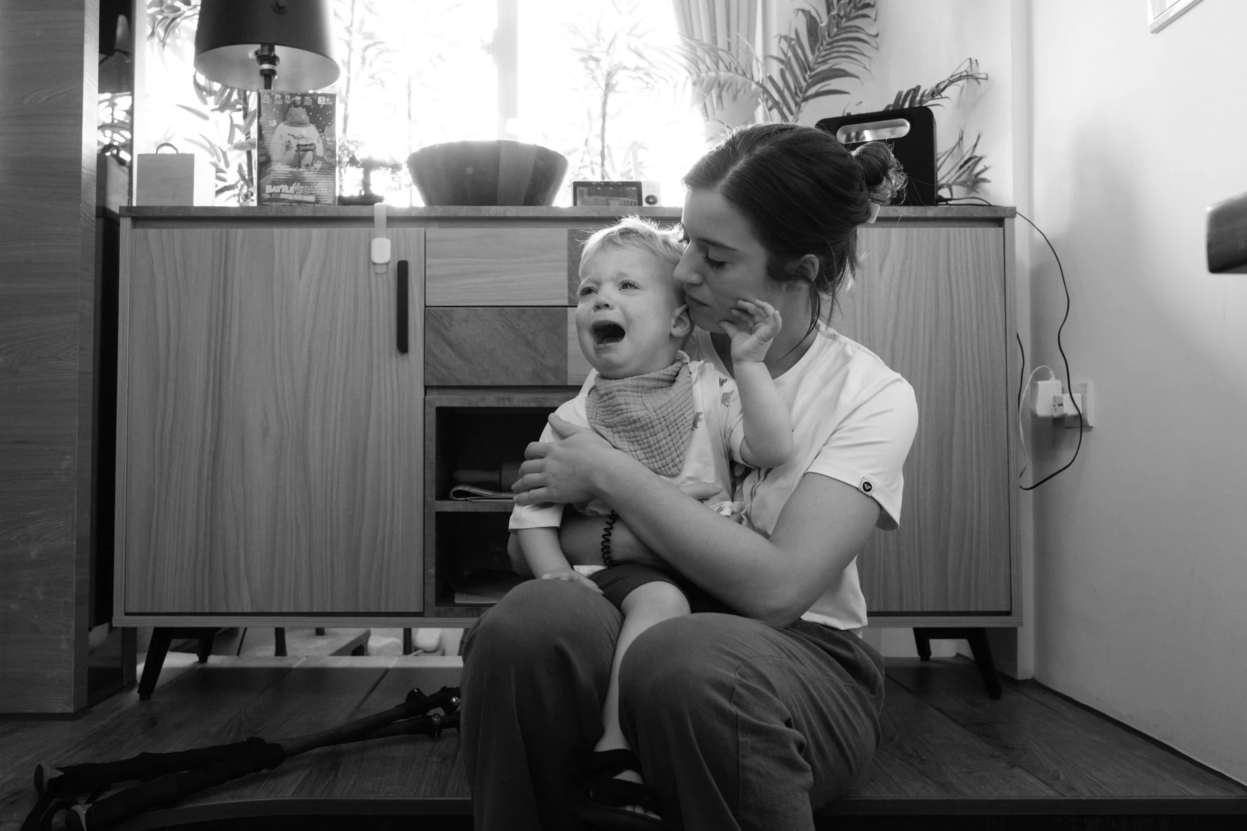 A mother comforts her crying child on the floor of their Taipei apartment during a day in the life documentary family photography session in Taiwan.