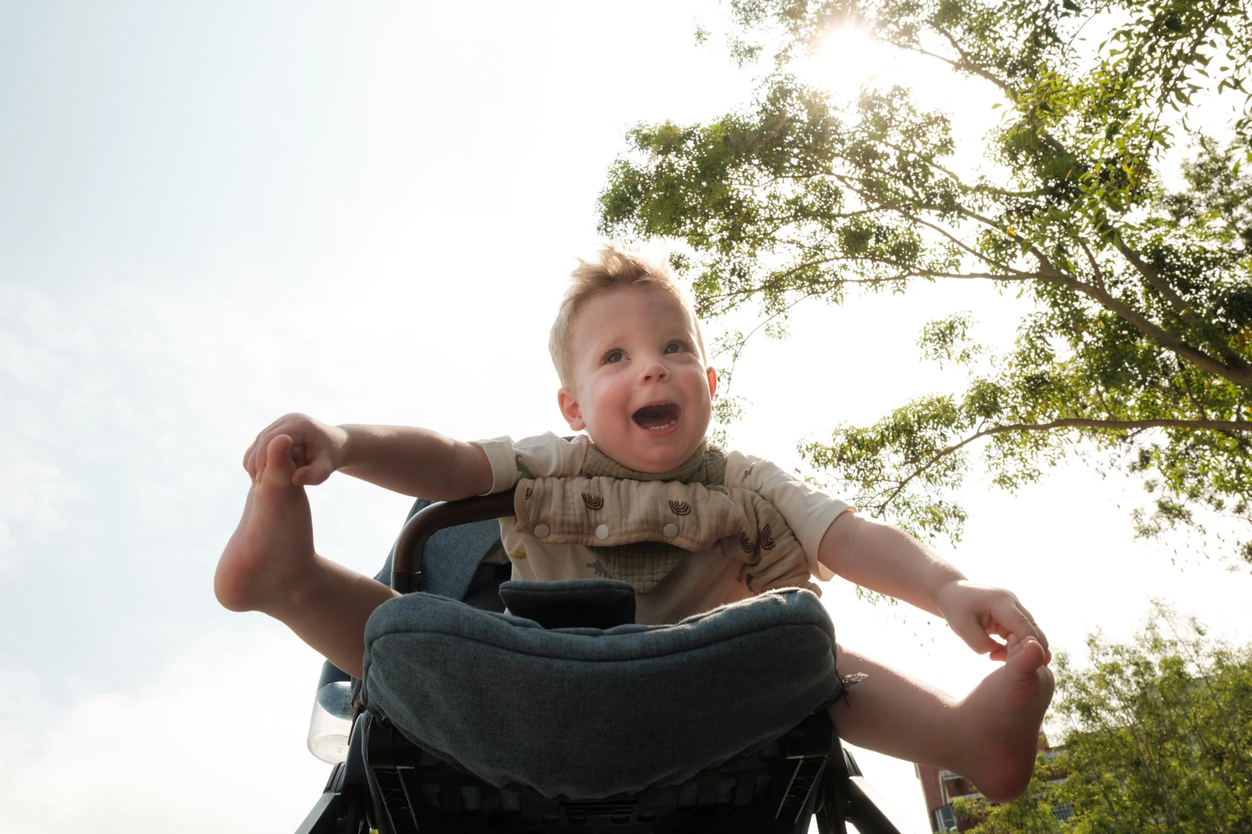 A little boy grabs his feet and smiles as he sits in his stroller outside in Taipei during an outdoor family photography session.