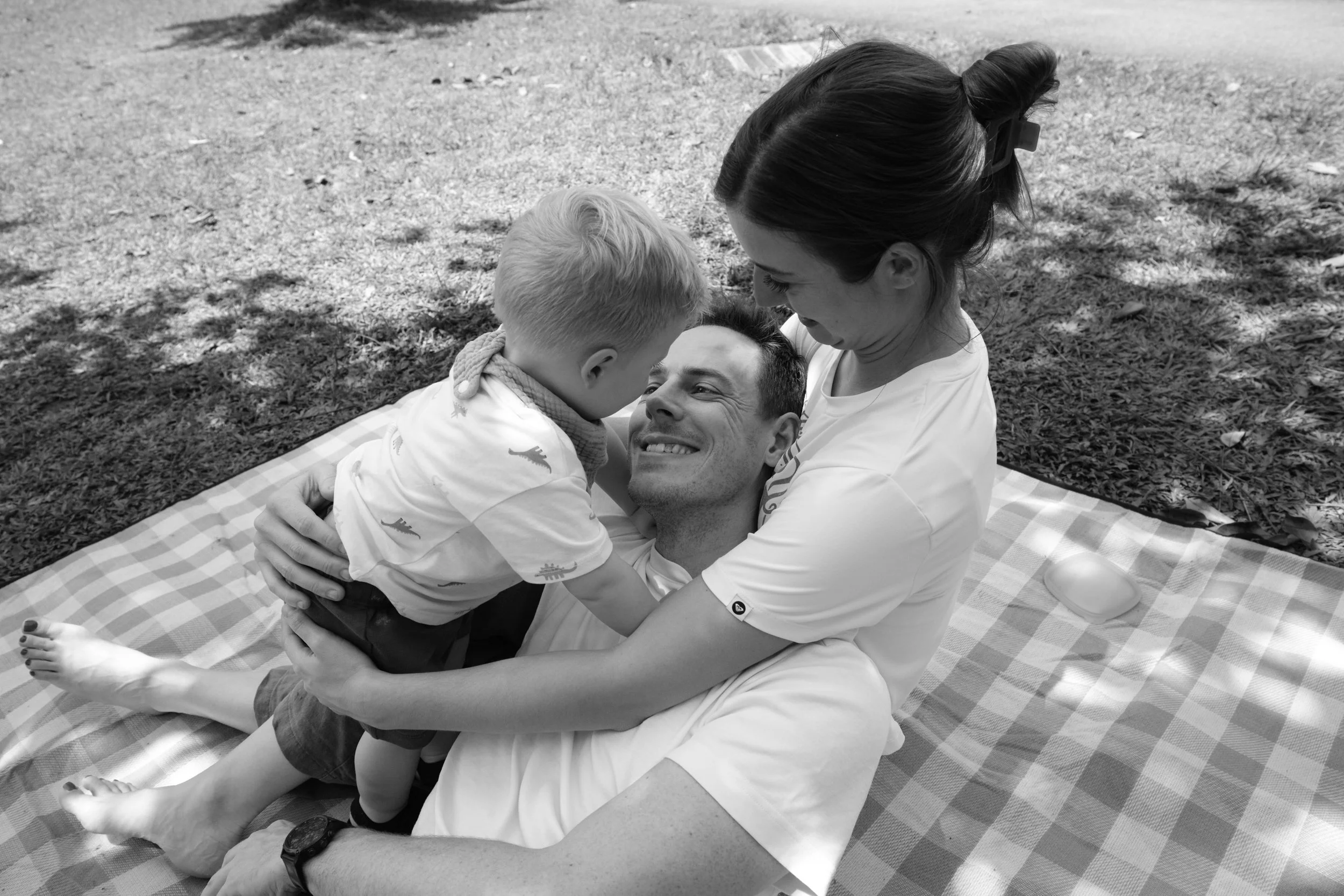 A little boy is crawling on top of his father and mother on a picnic blanket in Daan park in Taipei during an outdoor family photography session.