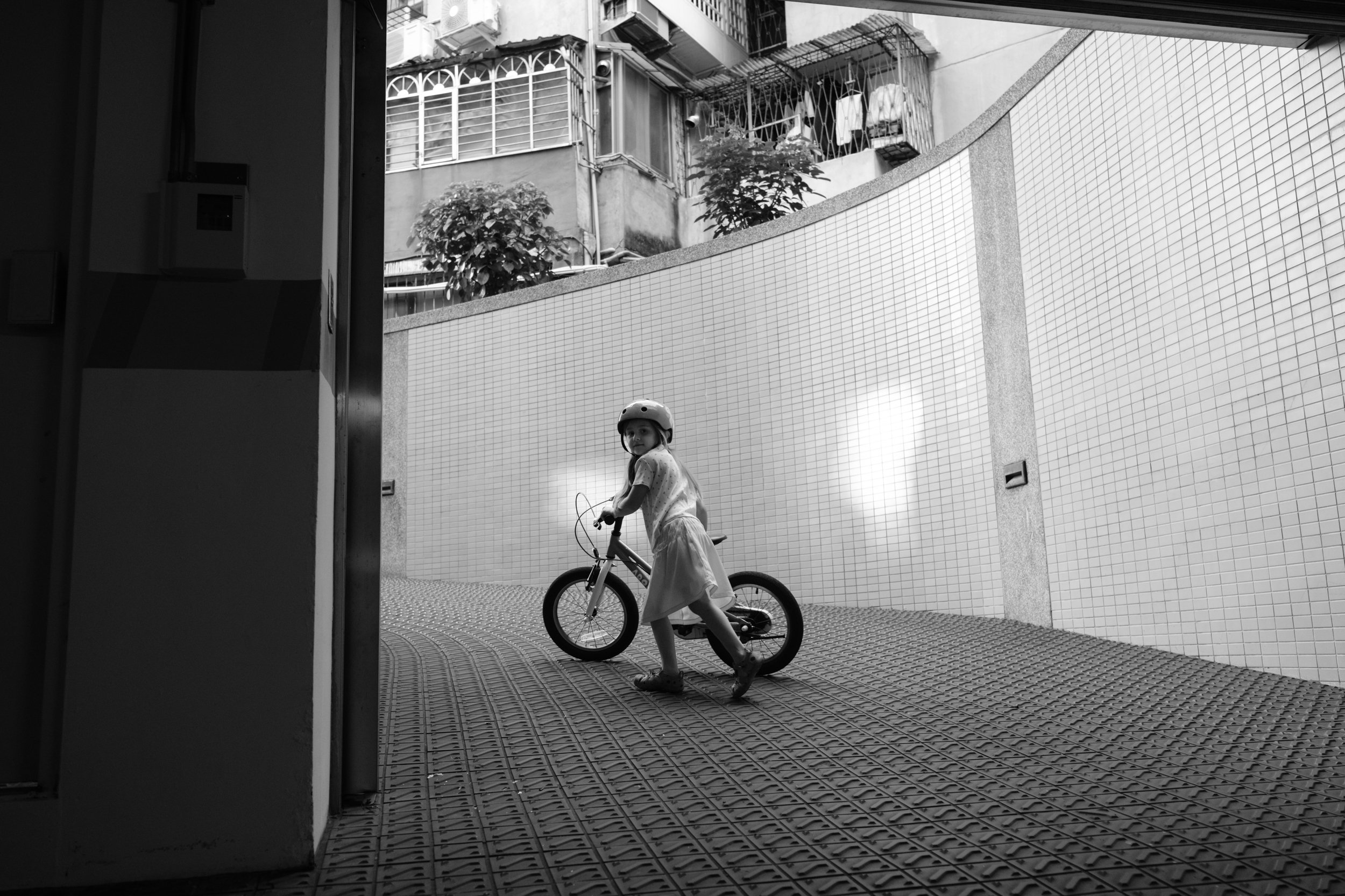 Taipei documentary family photography, Tienmu alley | Young girl on a balance bike glances back down a tiled residential passageway