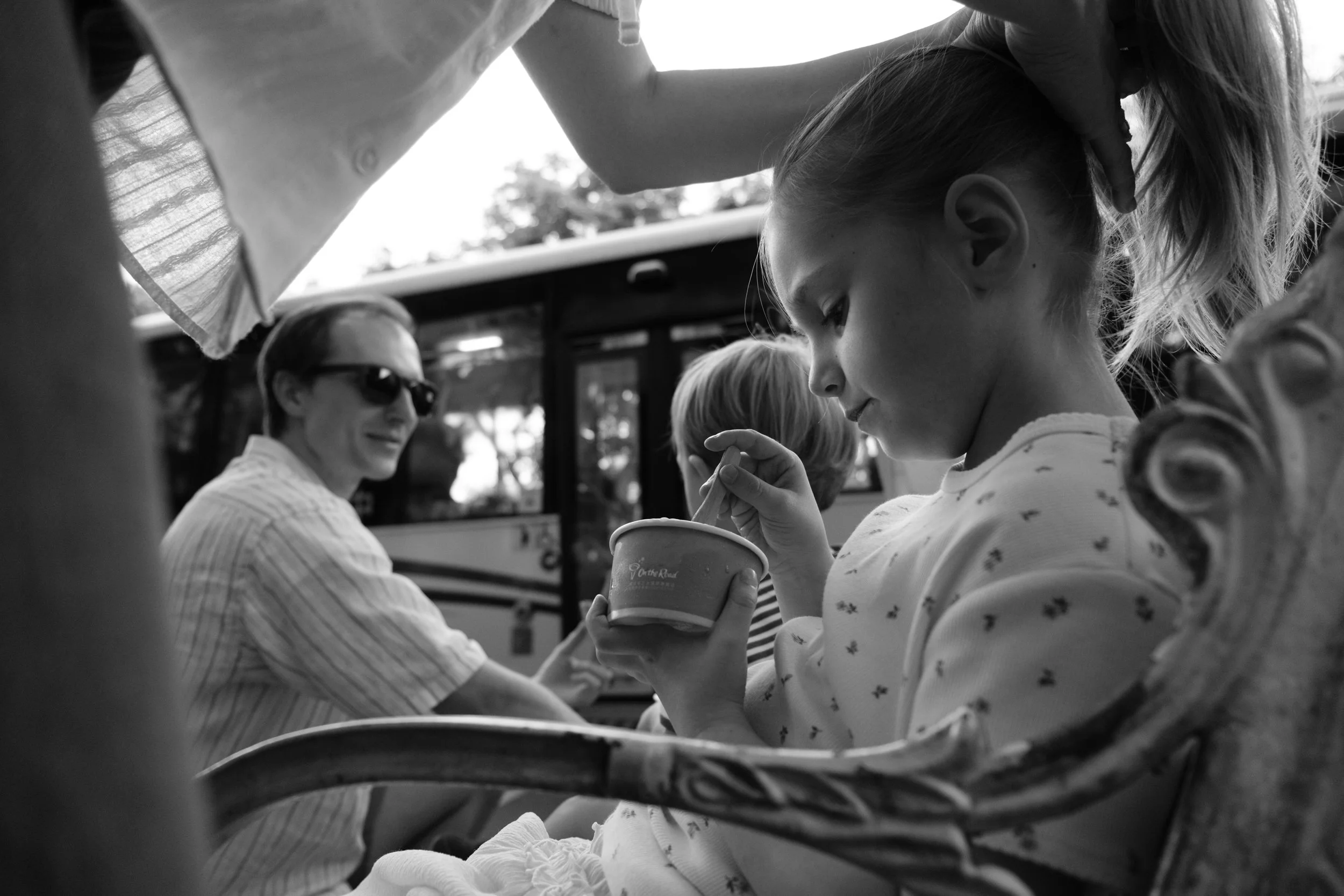 Taipei documentary family photography, Tienmu | Siblings share gelato outdoors while their father looks on, seated next to them on a bench