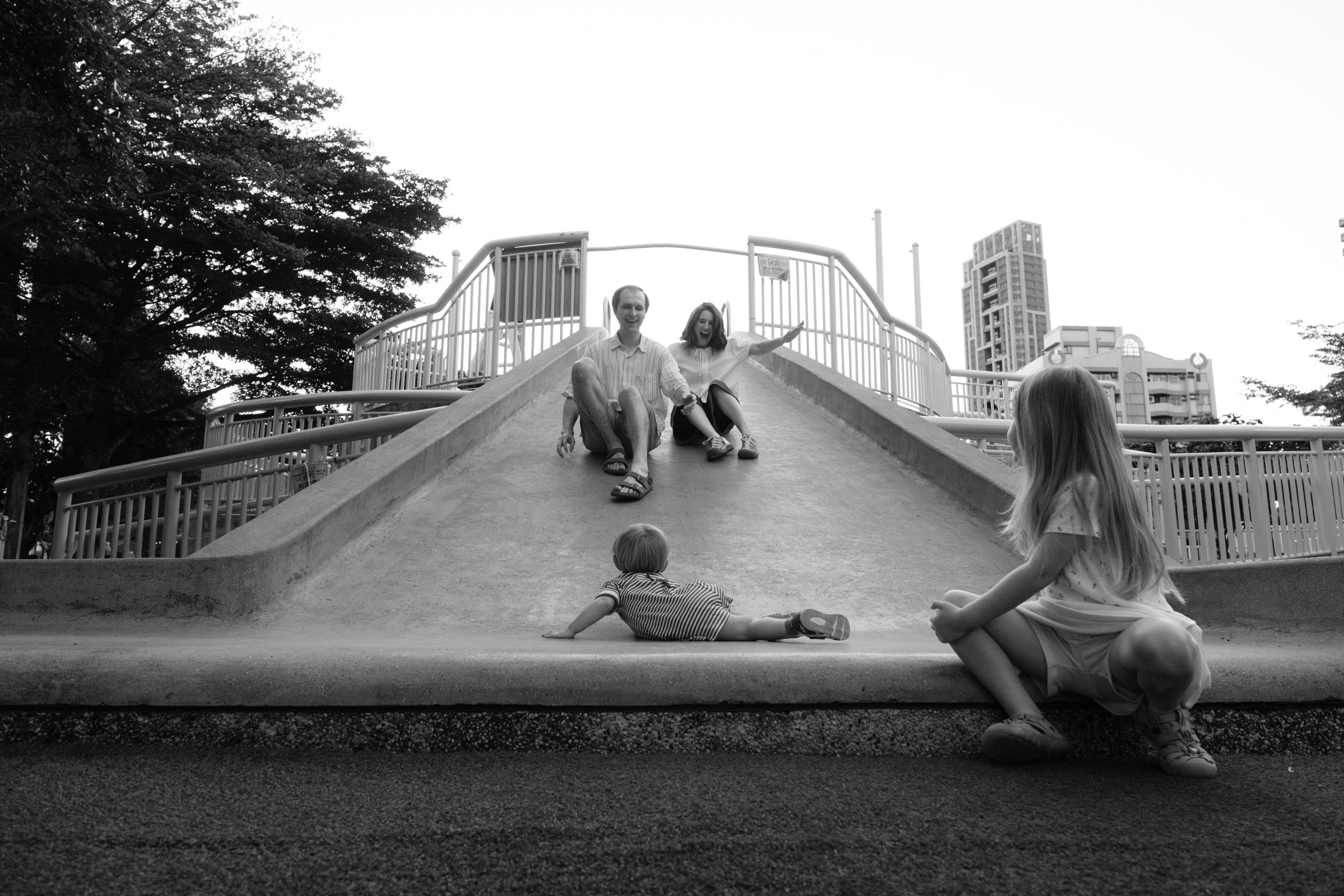 Taipei documentary family photography, Tienmu Sports Park | Parents slide down a concrete playground slide together as their children watch from below