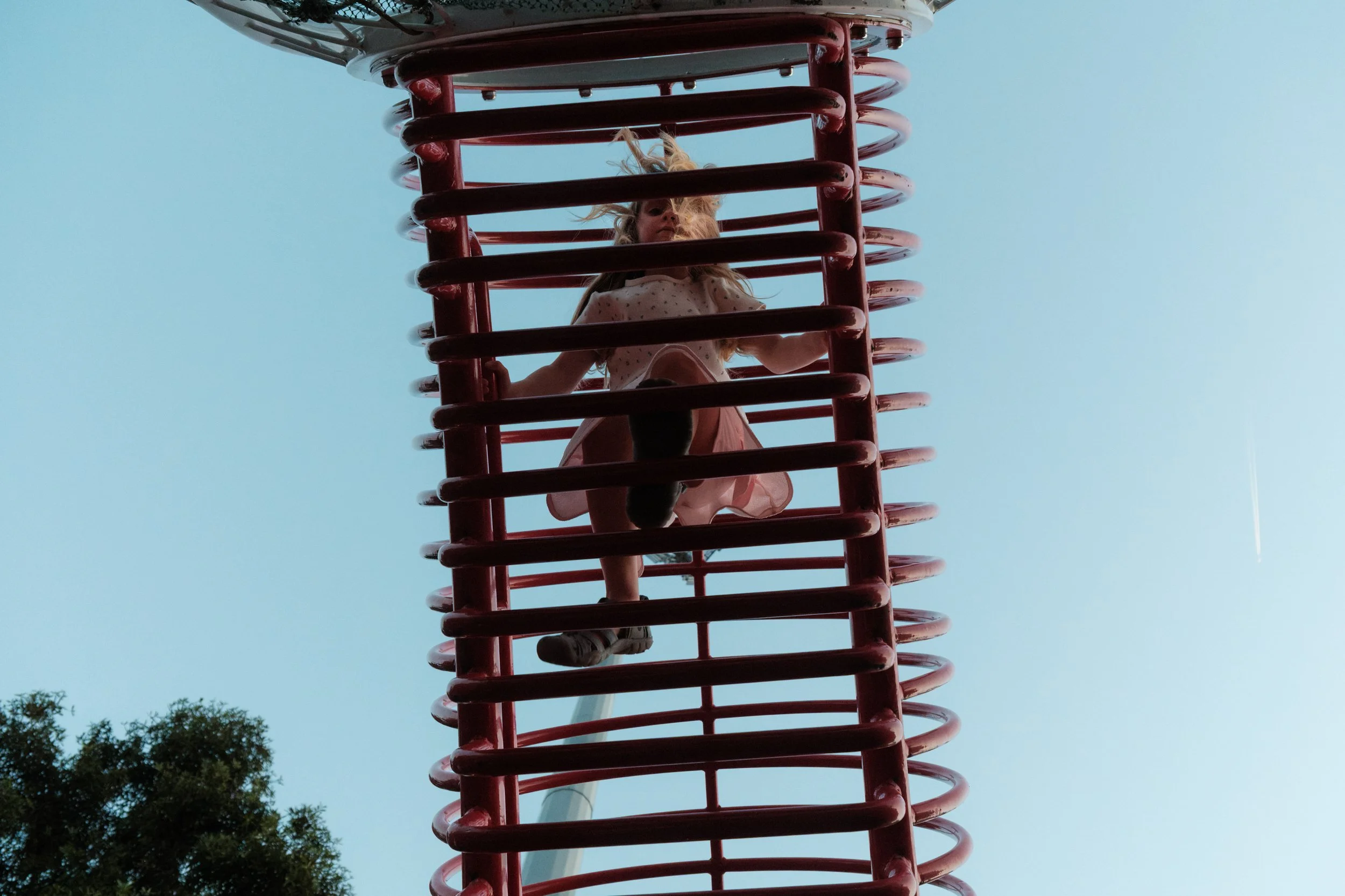 Taipei documentary family photography, Tienmu Sports Park | Girl climbs through a spiral tunnel climbing structure against the evening sky