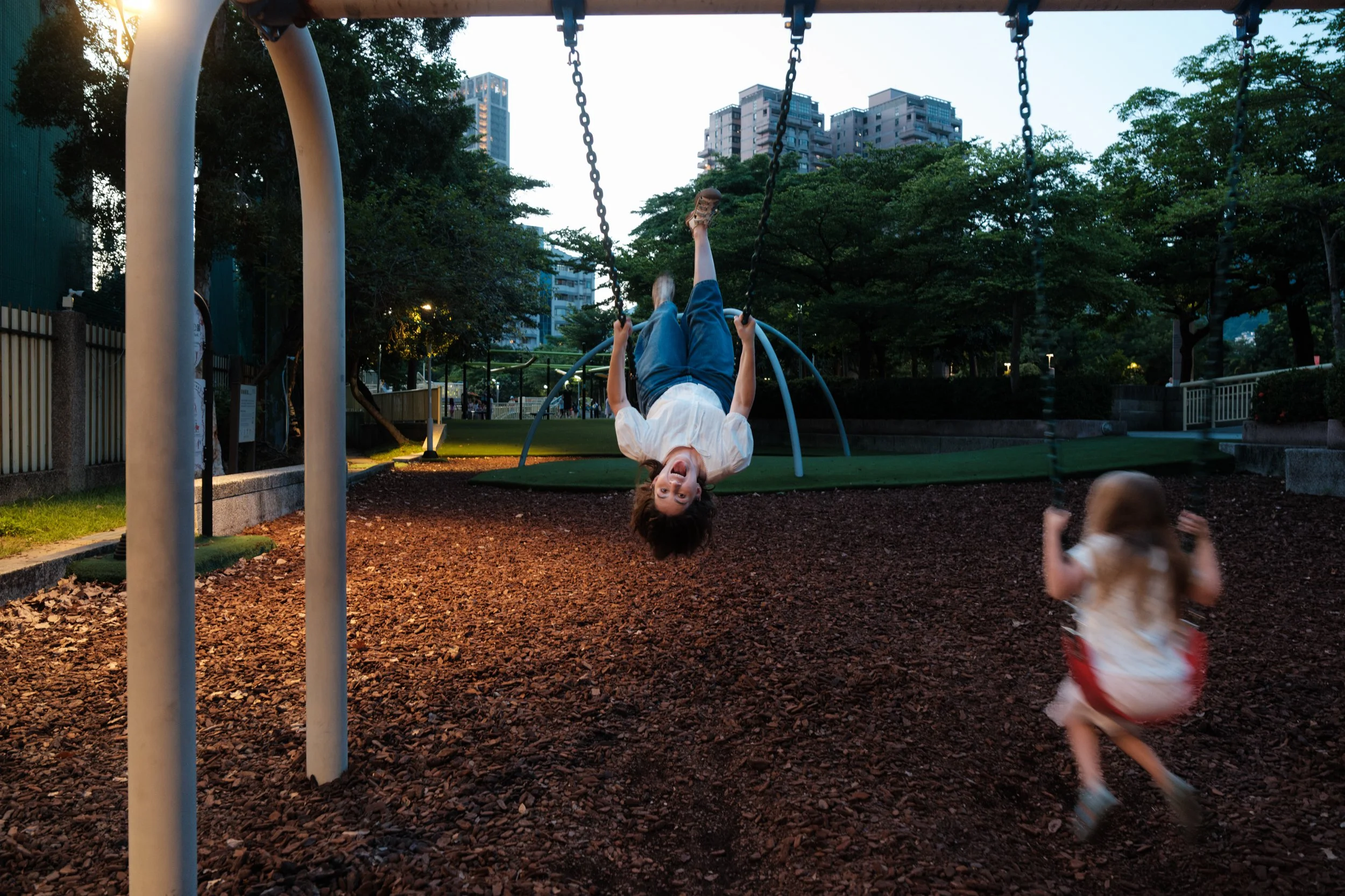Taipei documentary family photography, Tienmu Sports Park | Mother hangs upside down from a swing while her daughter swings nearby