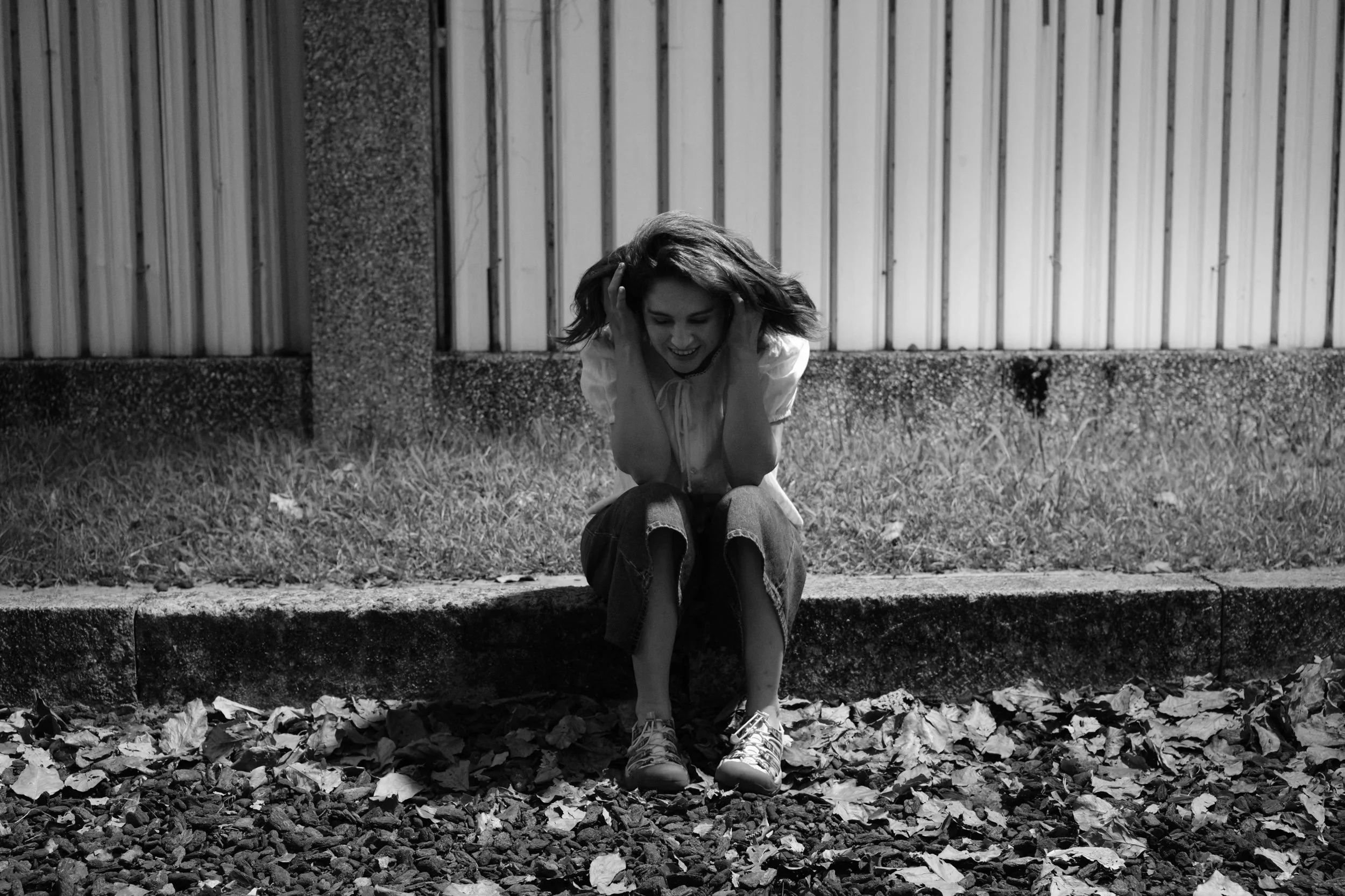 Taipei documentary family photography, Tienmu | Mother laughs while running her hands through her hair, seated on a curb scattered with fallen leaves