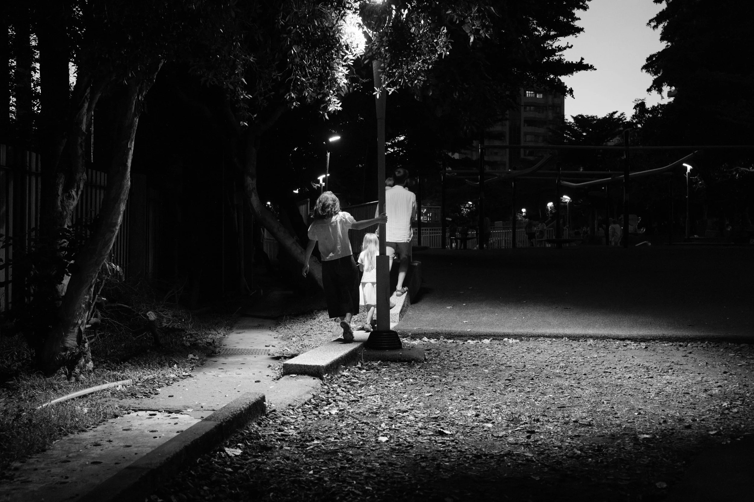 Taipei documentary family photography, Tienmu Sports Park at night | Family silhouetted walking together beneath a lamppost as evening settles over the park