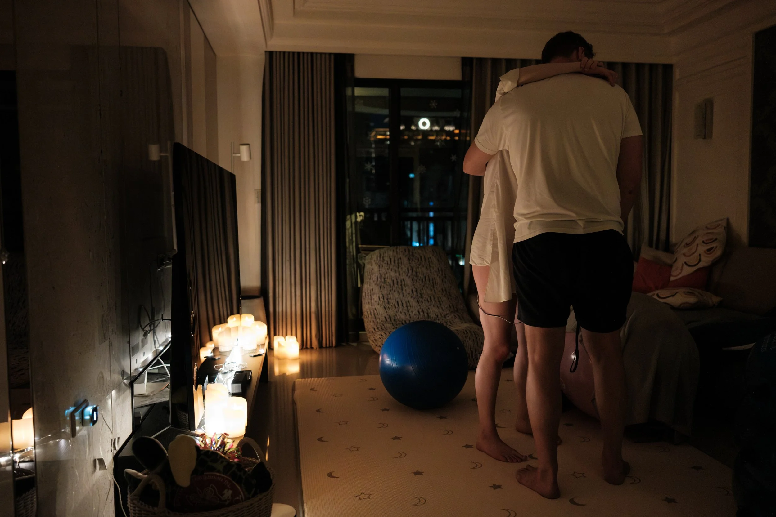 Expecting couple embracing during early labor in a candlelit Taipei apartment before a home birth