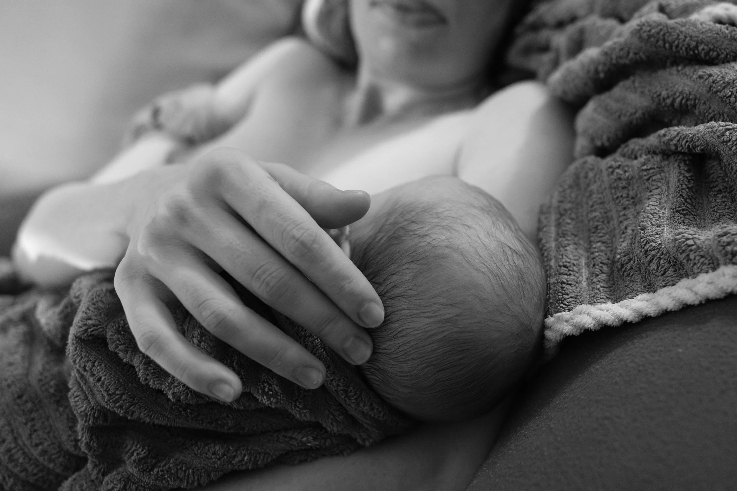 Mother's hand resting on her newborn's head moments after a home water birth in Taiwan