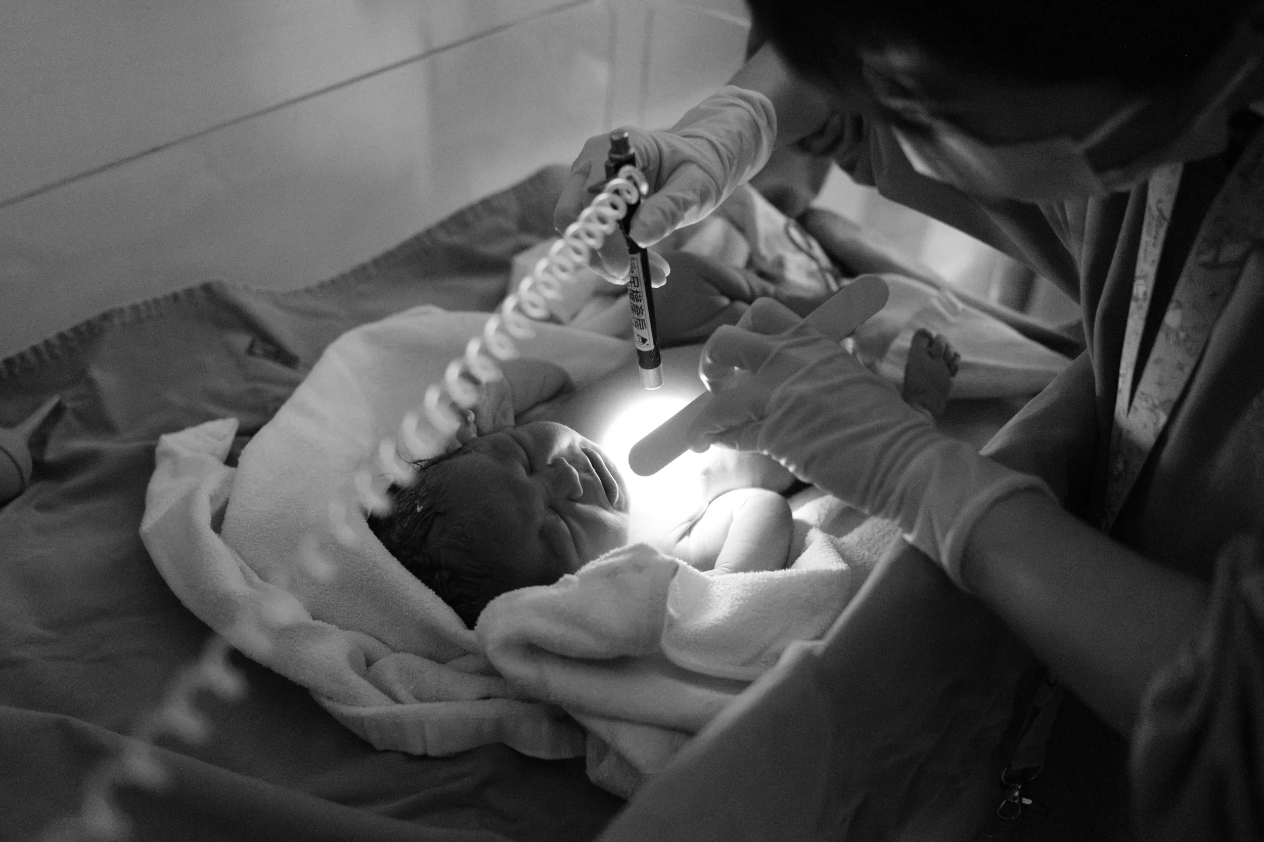 Newborn exam after a water birth at Dianthus in Taipei, Taiwan — nurse checking reflexes with a penlight on the warming table.