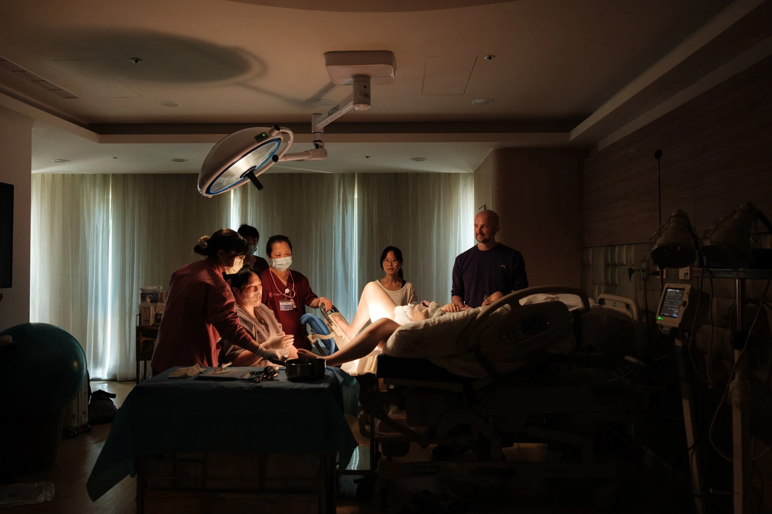 Wide shot of a delivery room at Dianthus in Taipei, Taiwan, documenting the birth team, mother, and partner after labor.