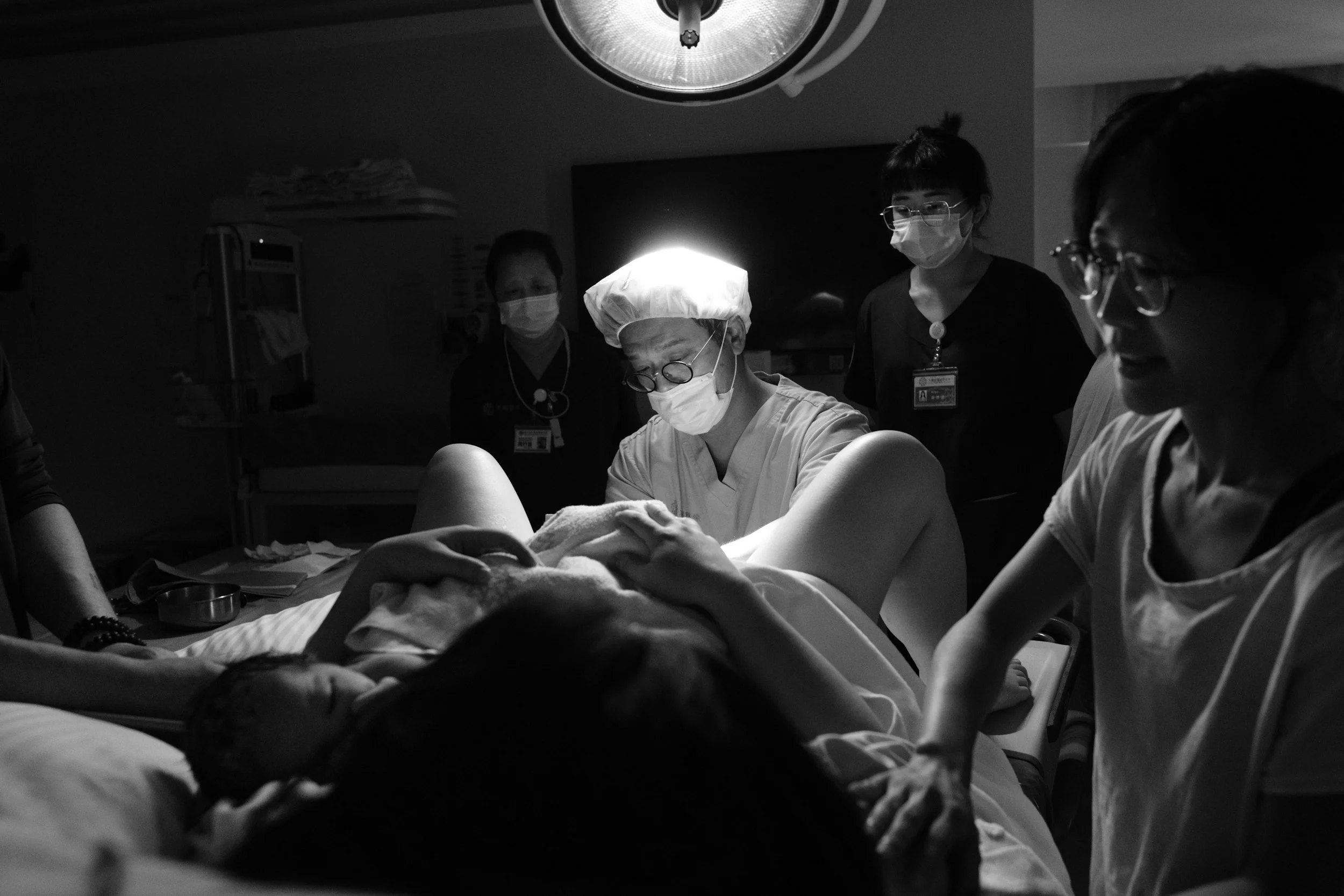 Birth photography at Dianthus, Taipei — doctor assisting delivery as family looks on.