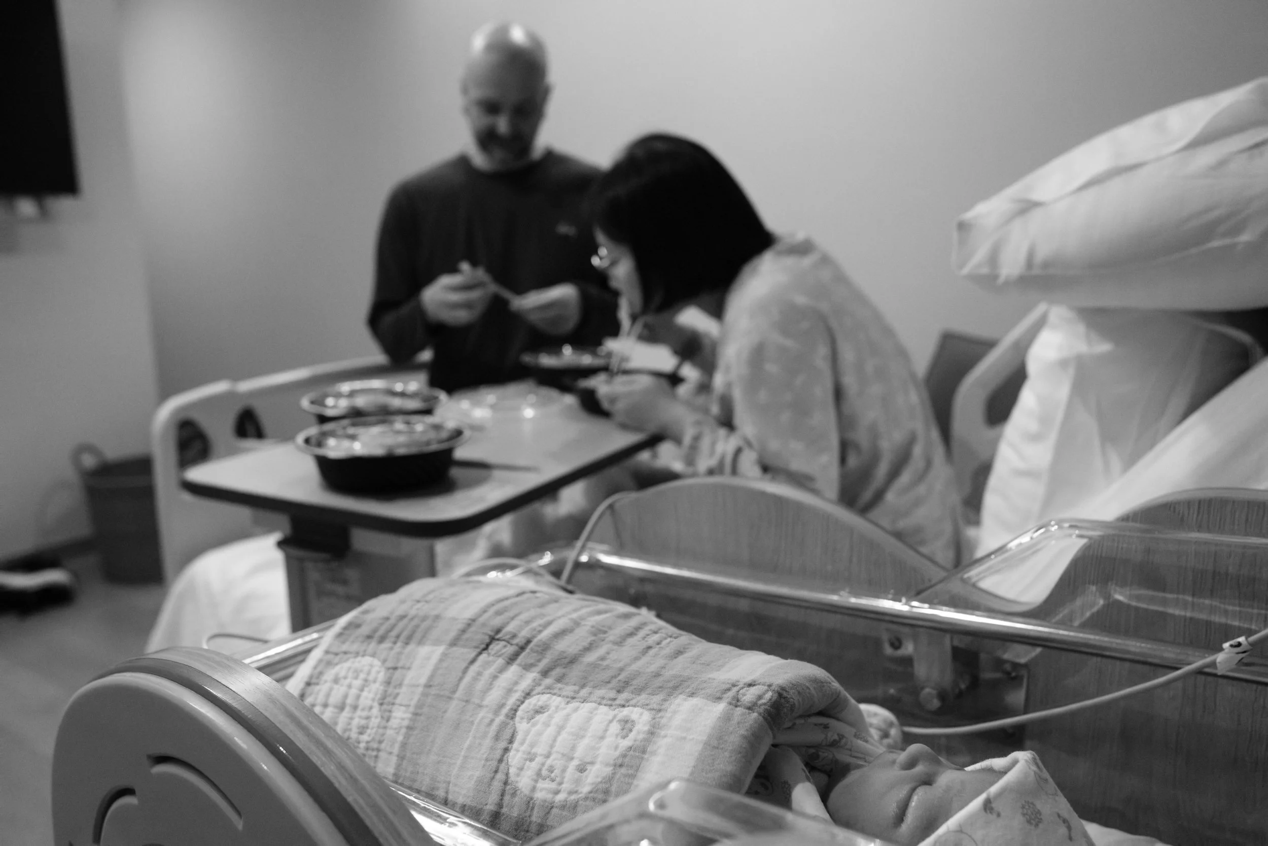 Birth photography at Dianthus, Taipei, Taiwan — parents sharing a meal while their newborn sleeps in the bassinet beside them.