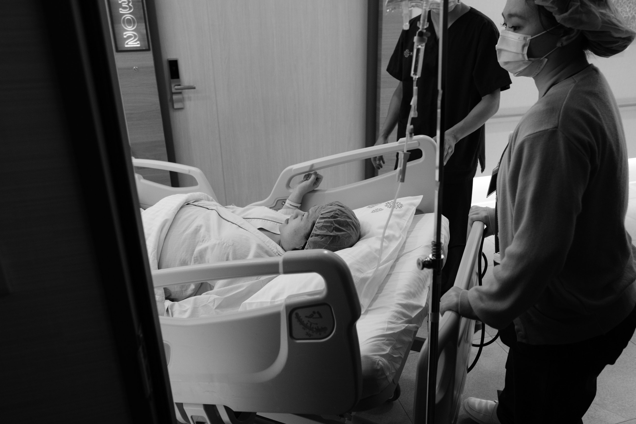Taipei c-section birth photography — mother lying on hospital bed being wheeled toward the operating room, medical staff walking alongside.