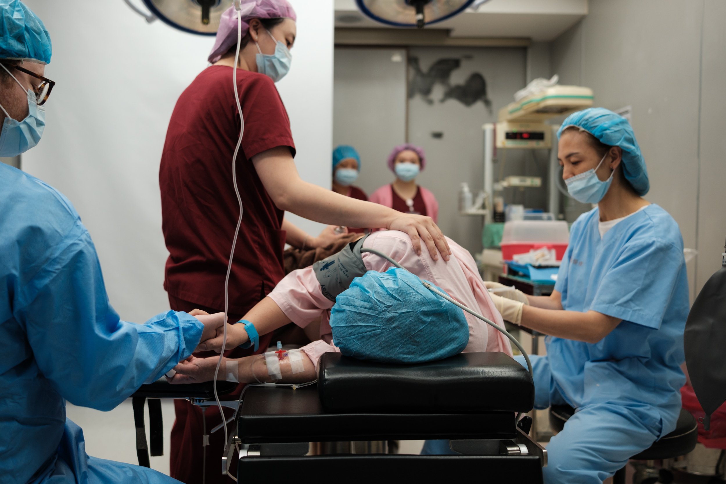 C-section surgery in progress at Dianthus Taipei — surgical team supports mother's back as anesthesia is administered before delivery.